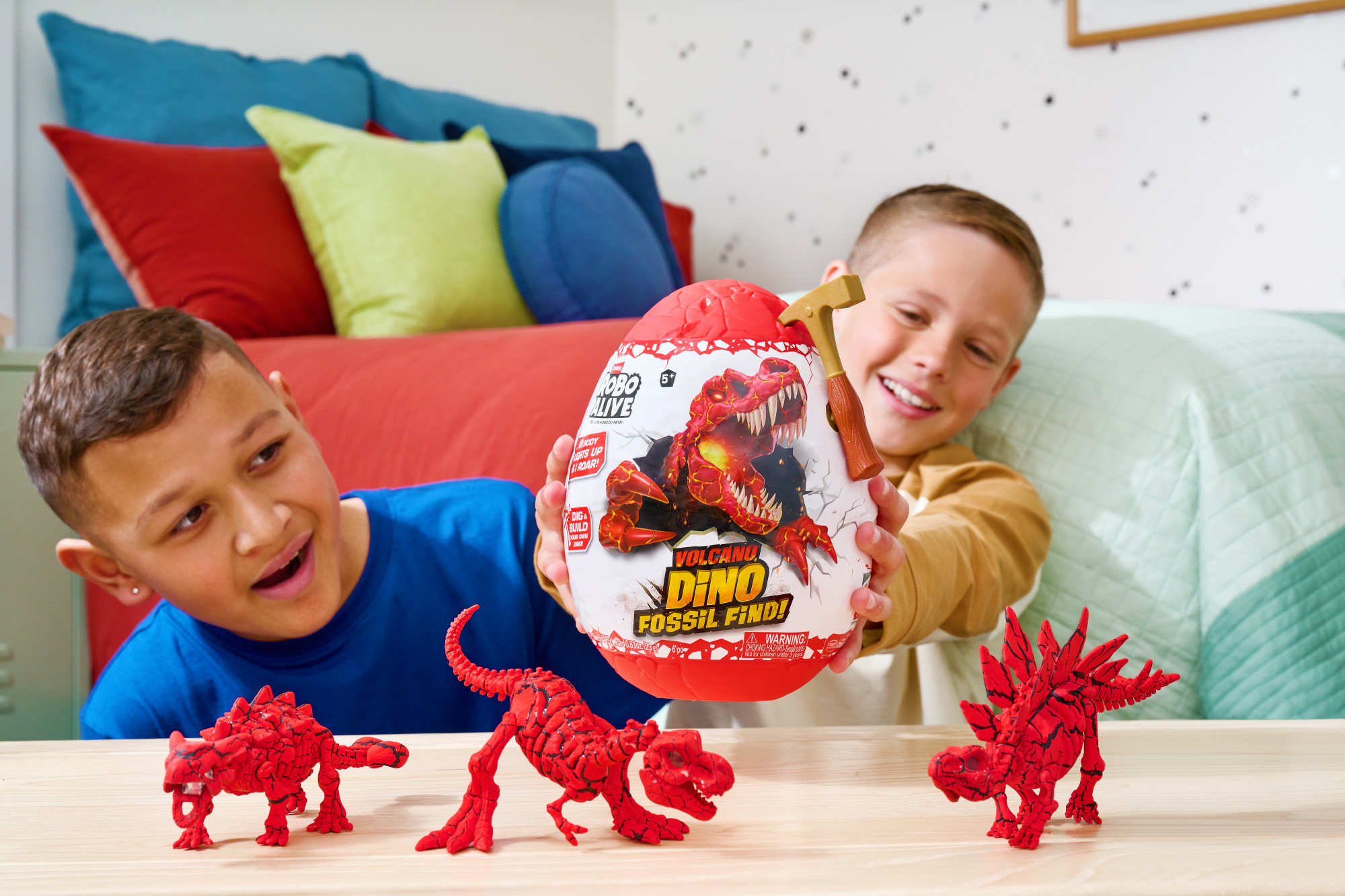 Dos niños con un huevo fósil de dinosaurio y dinosaurios de juguete. El huevo es rojo y blanco, con un martillo de juguete. Hay dinosaurios de juguete rojos en la mesa.