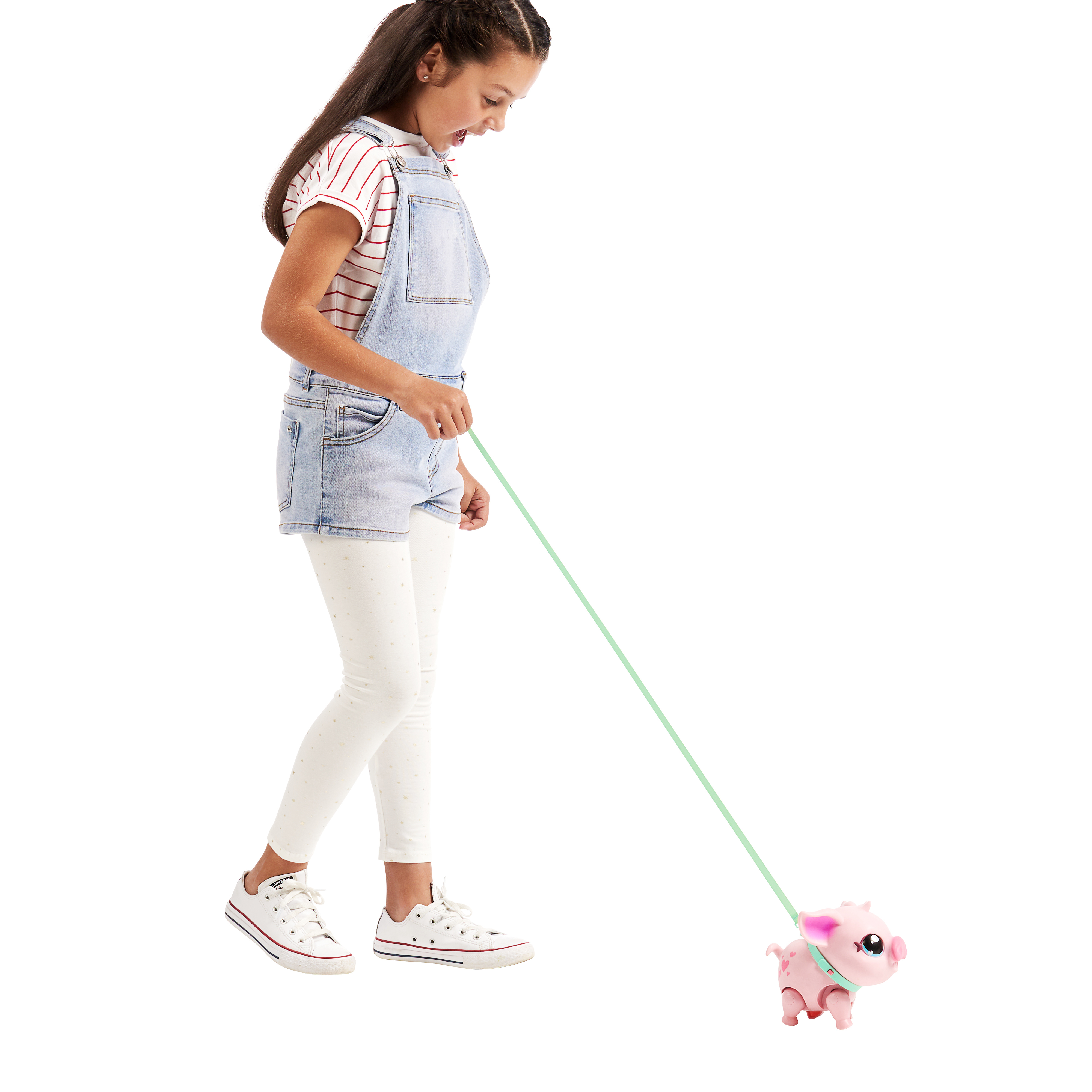 Ein Mädchen führt ein Spielzeugschwein an der Leine. Sie trägt eine Latzhose und Turnschuhe. Das Schwein ist rosa.
