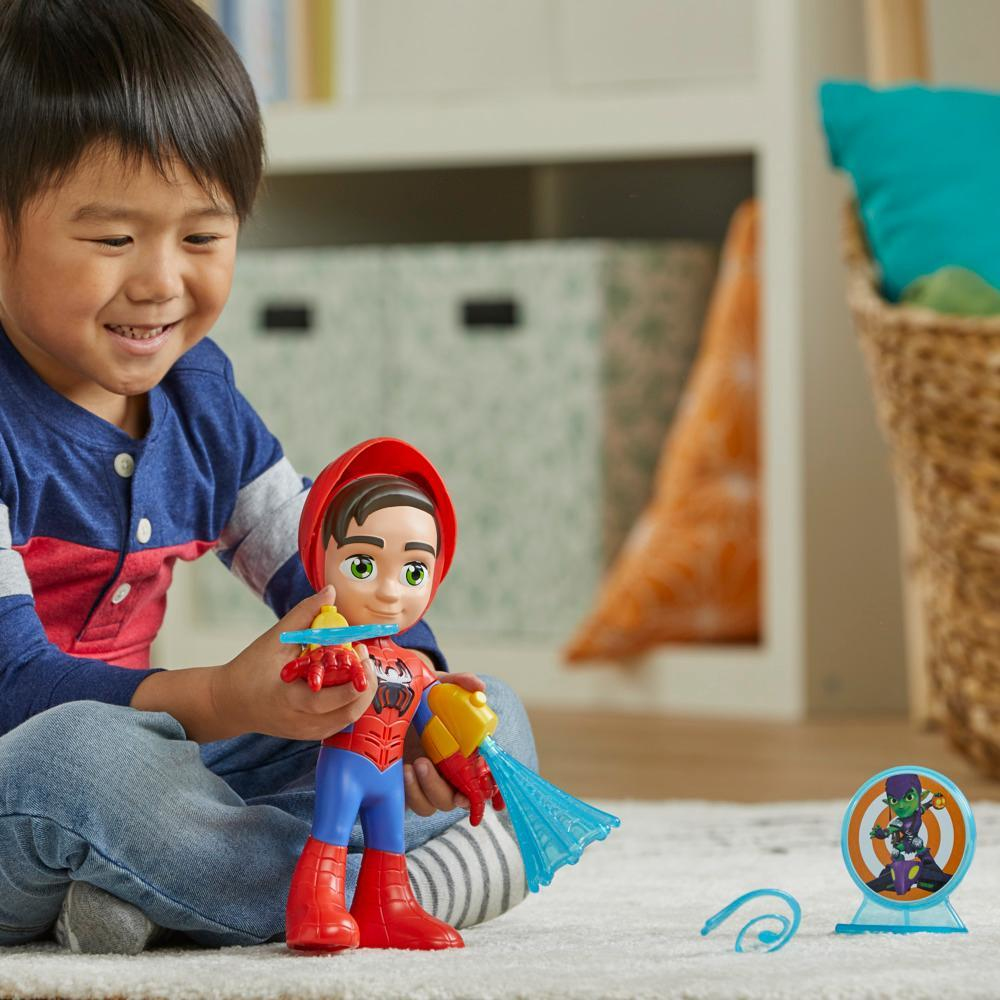 Un niño sonríe sosteniendo un juguete de Spider-Man. El juguete dispara agua azul. Un blanco con un personaje de dibujos animados está detrás.