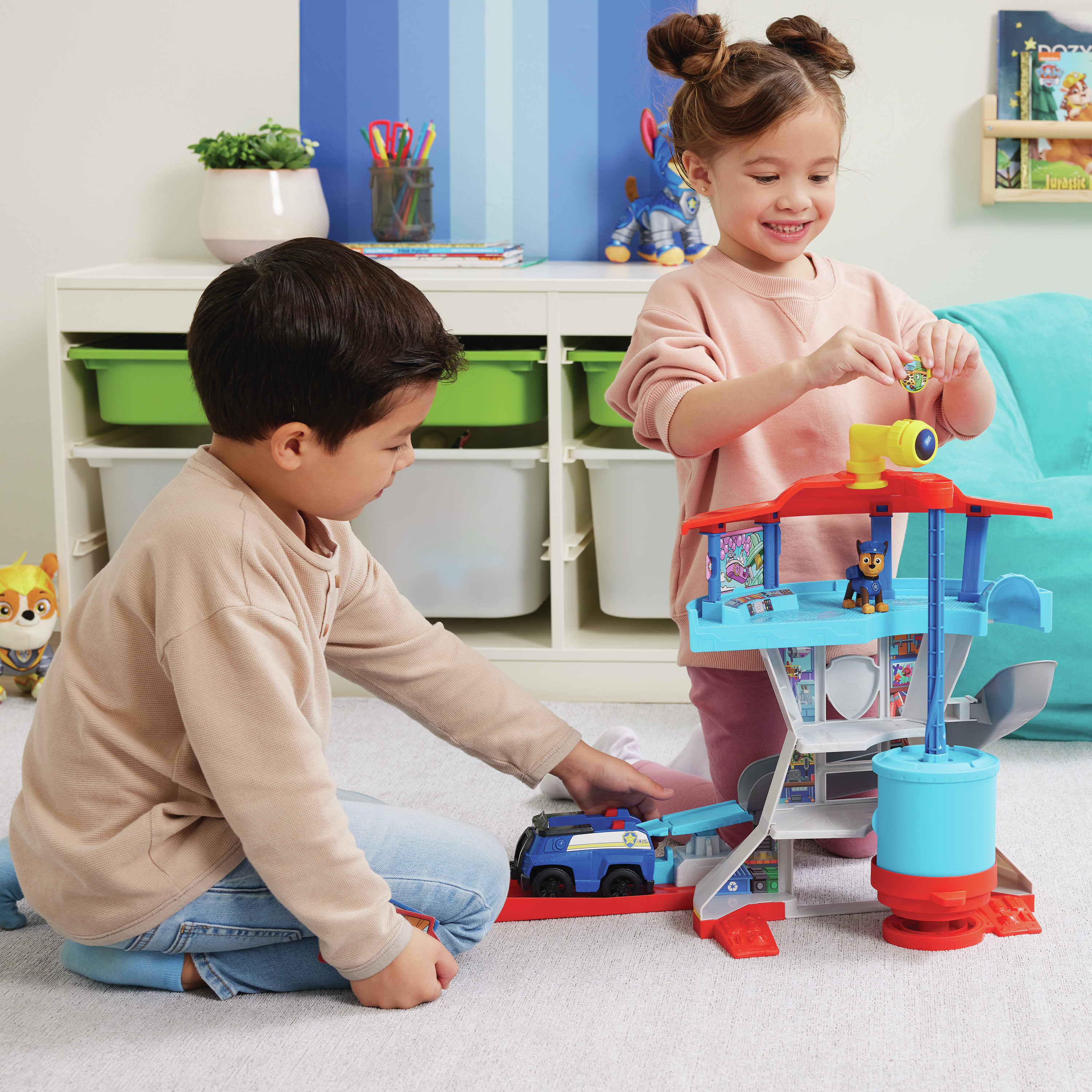 Due bambini giocano con un set di giocattoli Paw Patrol. Uno gioca con l'auto, l'altro con un gettone. La scena è al chiuso.