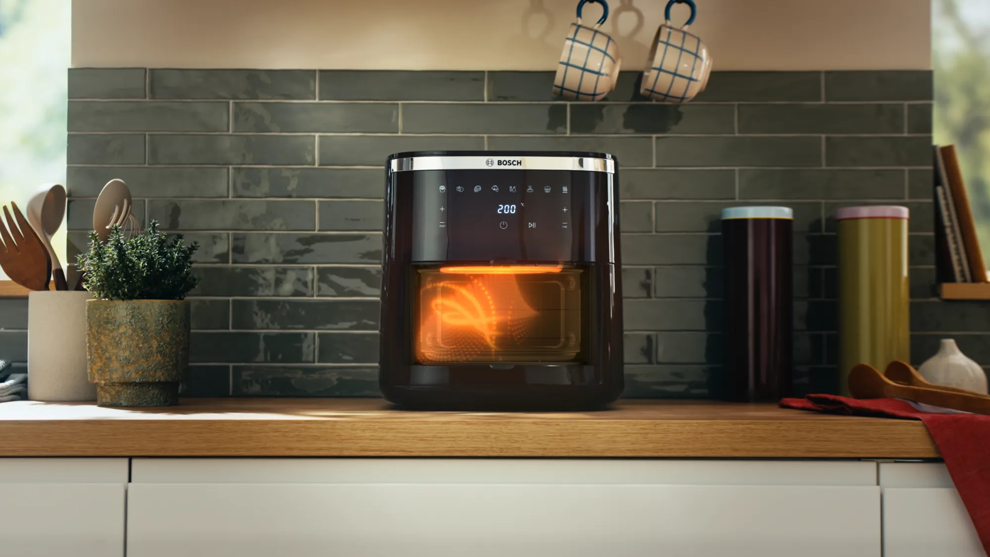 Frytownica beztłuszczowa stoi na drewnianym blacie. Są przybory kuchenne i roślina. W tle jest kafelkowa ściana i kilka kubków.