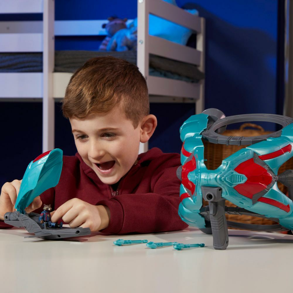 Un niño sonríe jugando con una nave espacial de juguete y una figura de Rocket Raccoon. También hay una pistola de juguete grande sobre la mesa. Una litera en el fondo.
