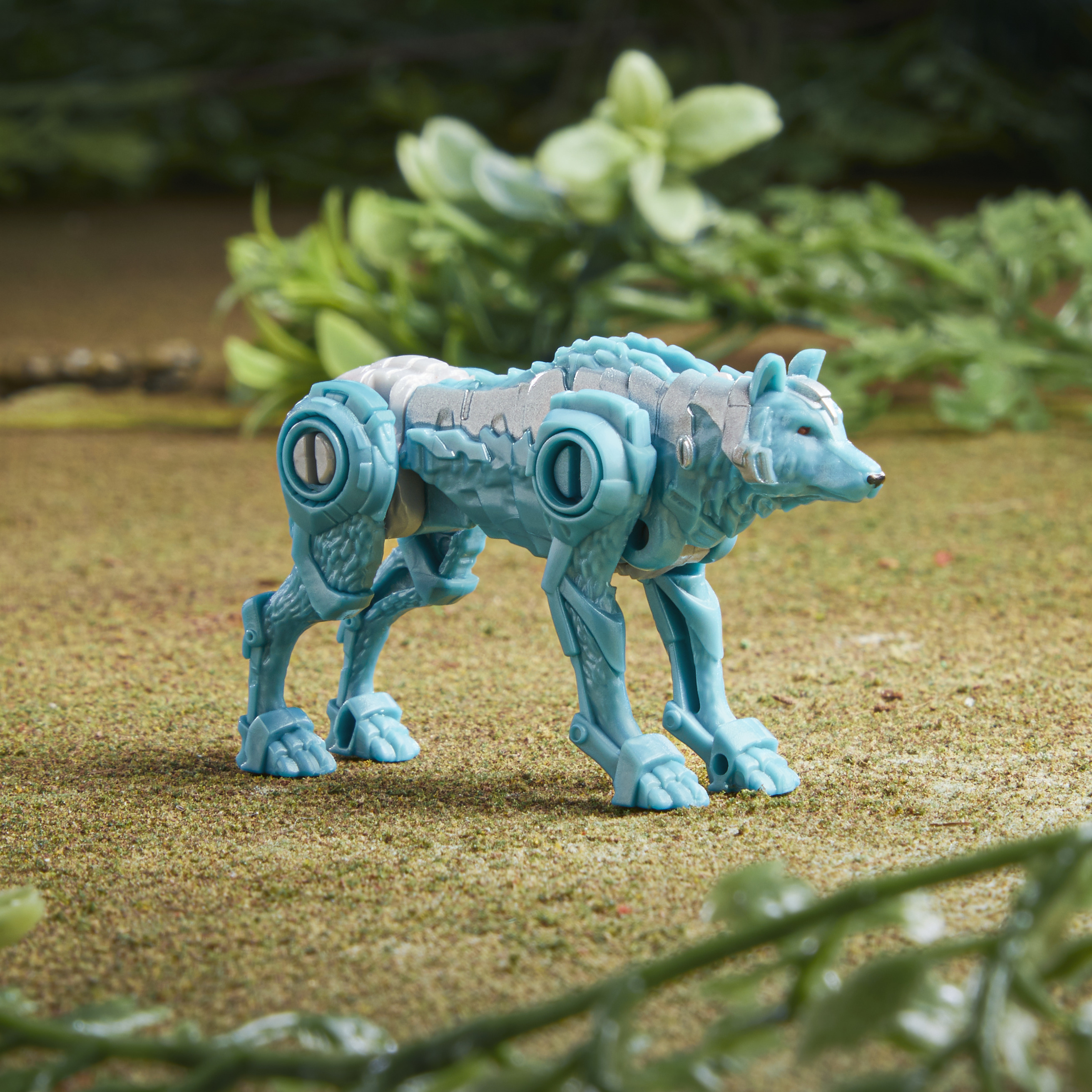 Niebieska zabawka w postaci wilka stoi na teksturowanej powierzchni, z zielonymi liśćmi w tle.