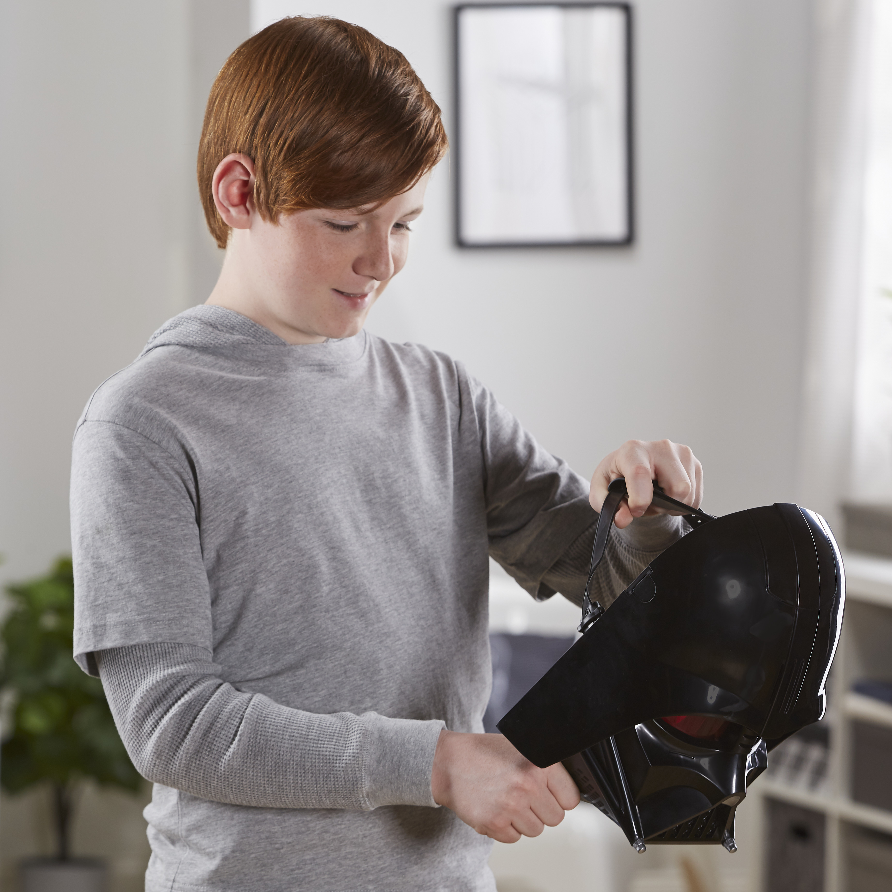 Un chico pelirrojo sostiene una máscara negra de Darth Vader. Está en una camisa gris, en interiores.