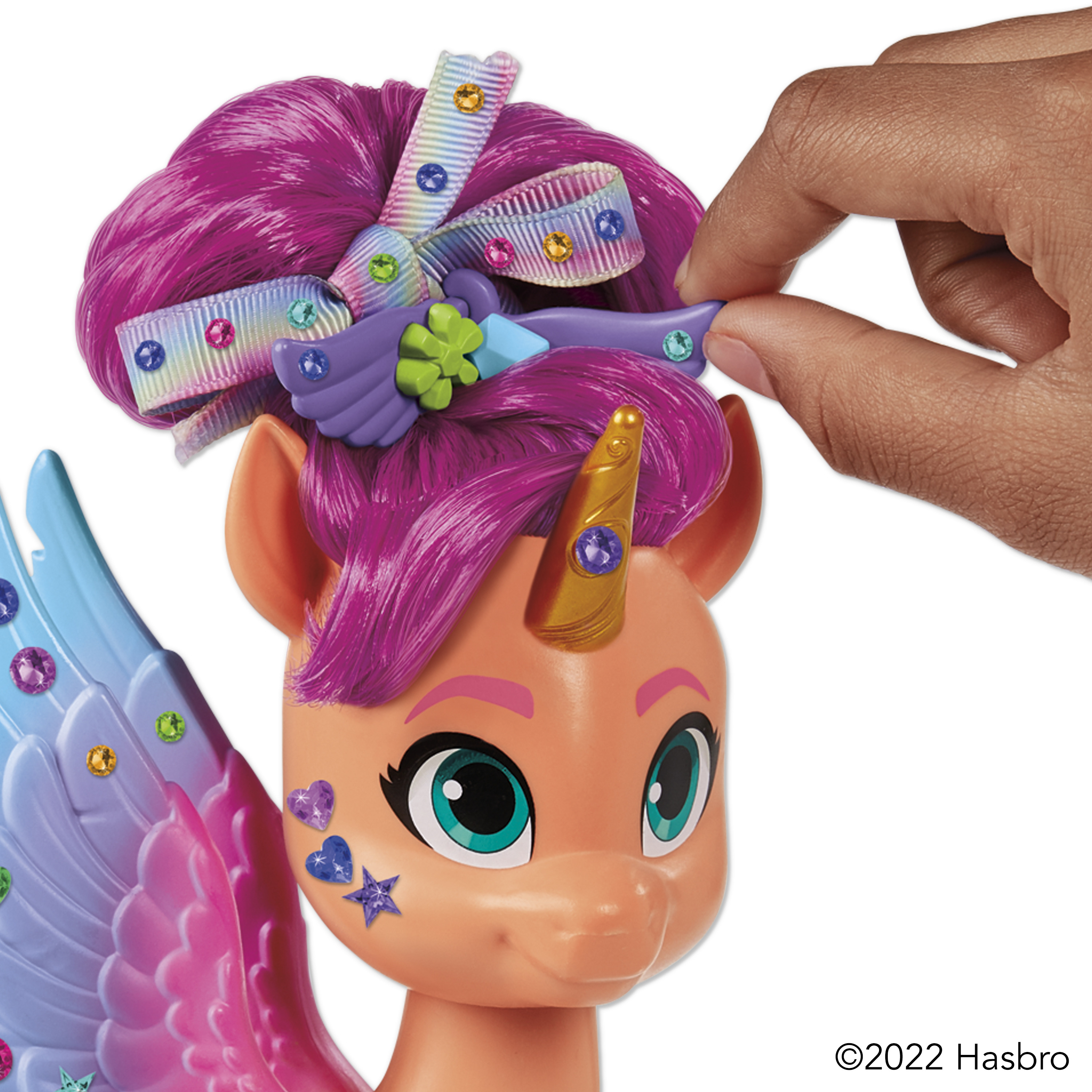 Unicornio de juguete con pelo morado y una mano ajustando su accesorio para el pelo. Tiene un cuerno y alas con gemas.