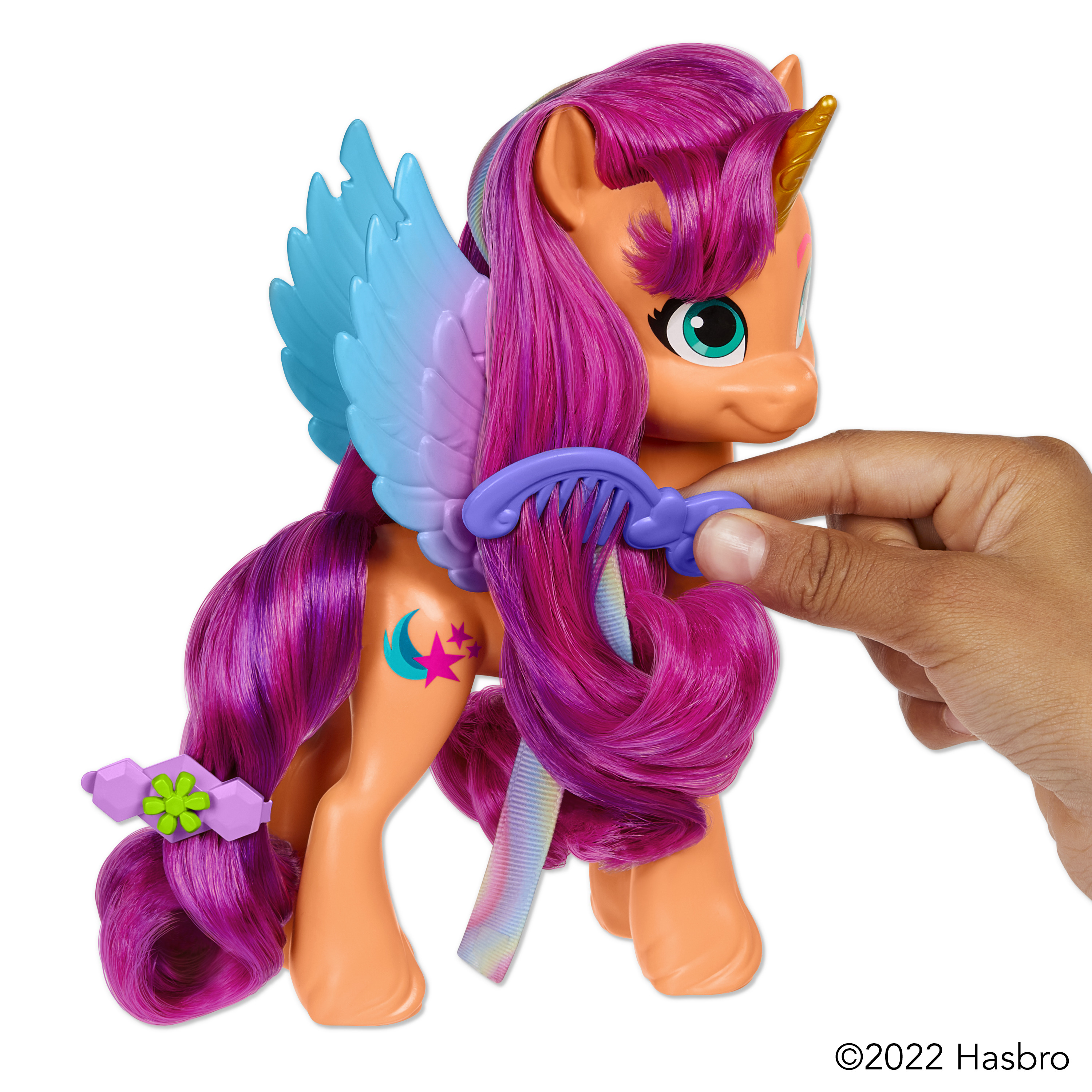 Un pony de juguete con piel naranja, pelo morado, alas azules y un cuerno dorado. Una mano sostiene el pony.