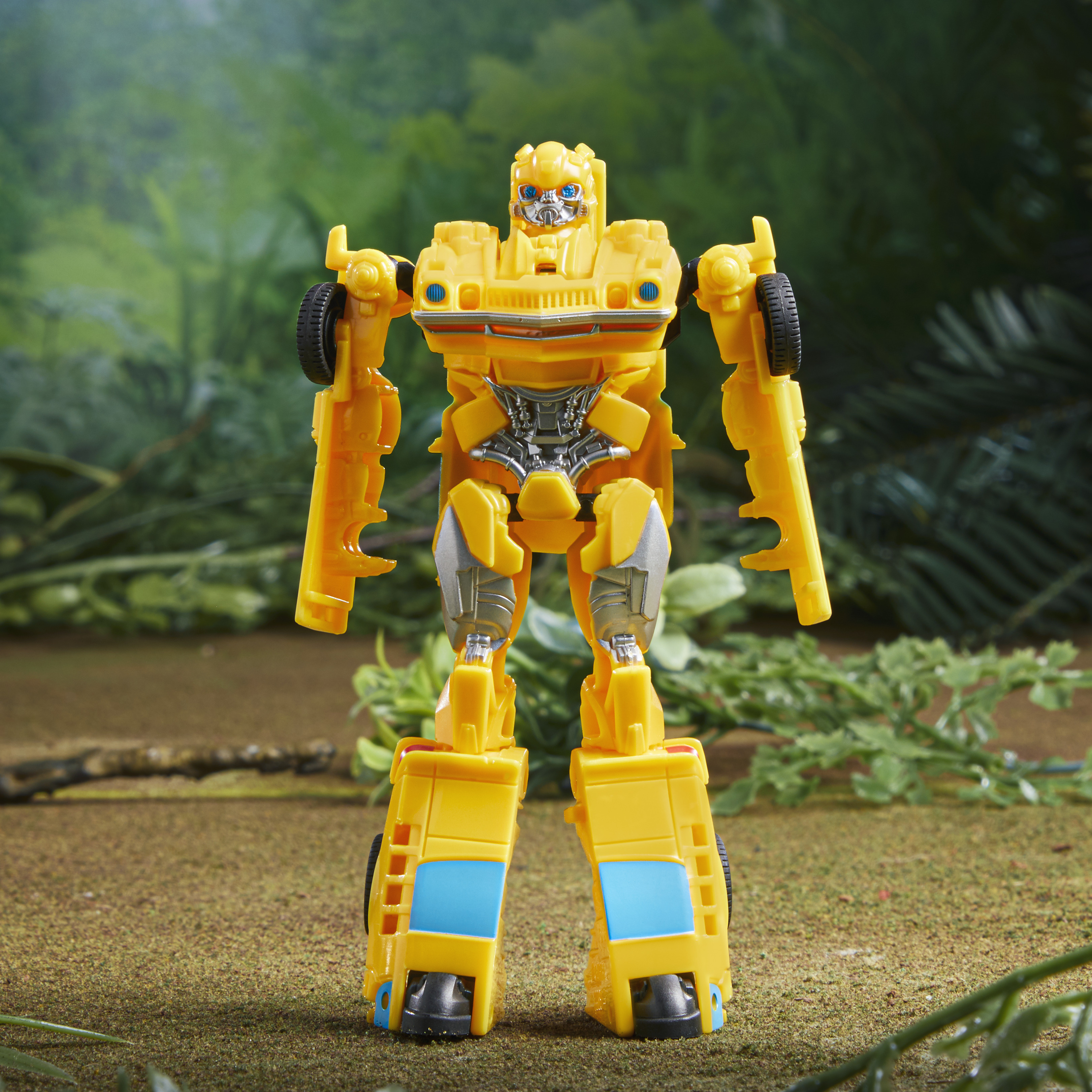Żółta zabawka transformera Bumblebee stoi na brązowej powierzchni z zielonym tłem z roślin i liści.