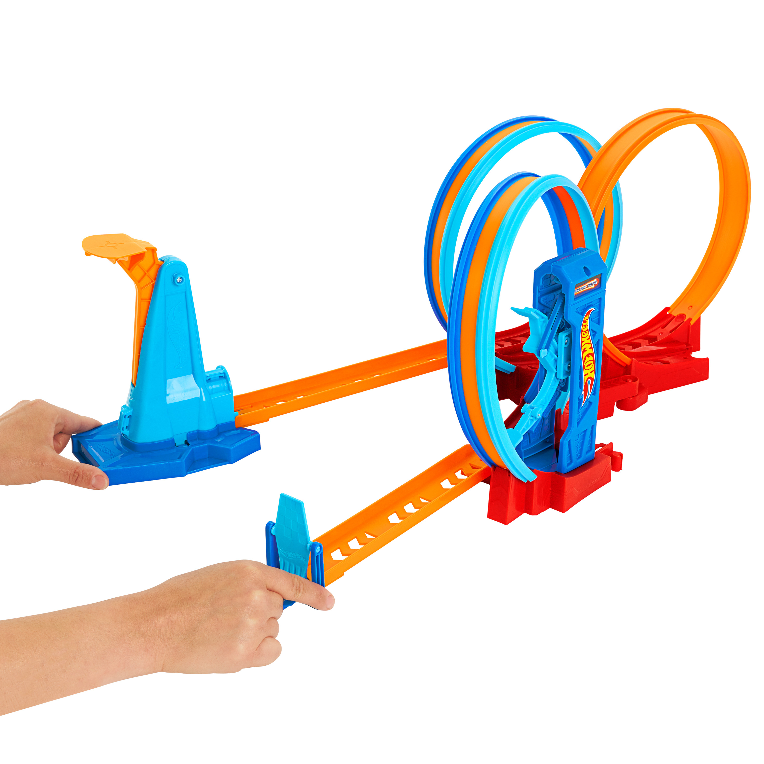 Zestaw torów Hot Wheels z pętlami i wyrzutnią. Ręce trzymają elementy toru. Kolory to niebieski, pomarańczowy i czerwony.