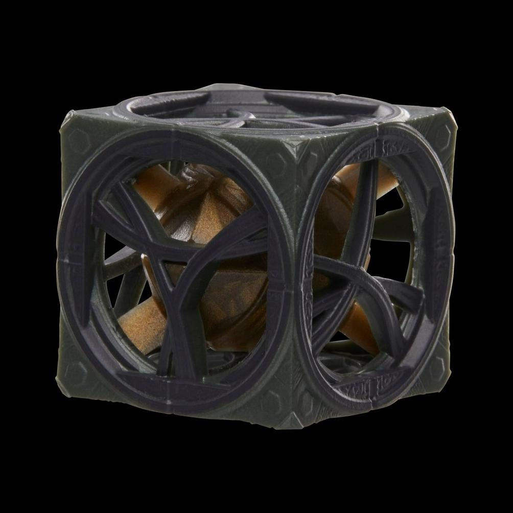 Obiekt w kształcie kostki z ciemnozieloną strukturą przypominającą klatkę. Wewnątrz widoczna jest złota kula. Tło jest czarne.