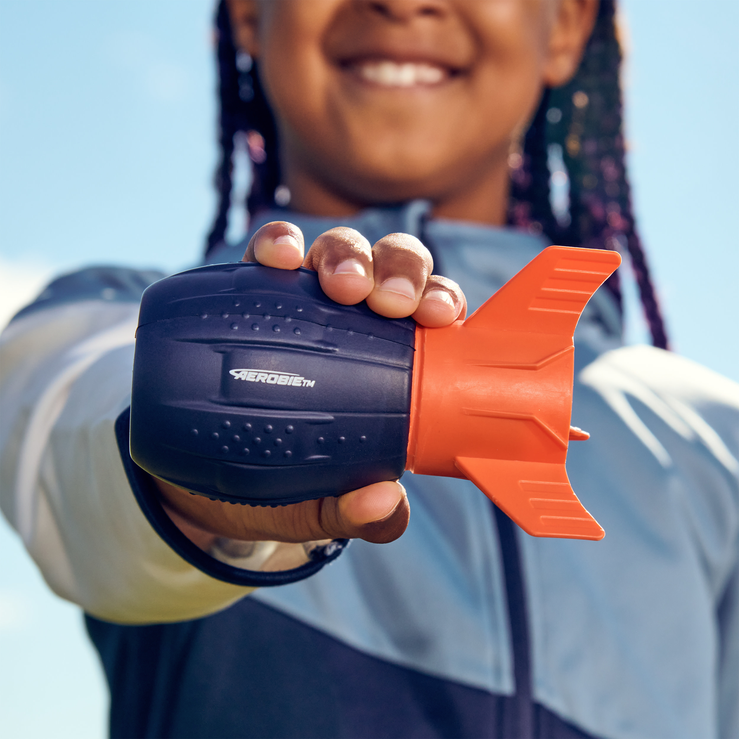 Osoba trzyma czarną i pomarańczową zabawkę. Tło to błękitne niebo.