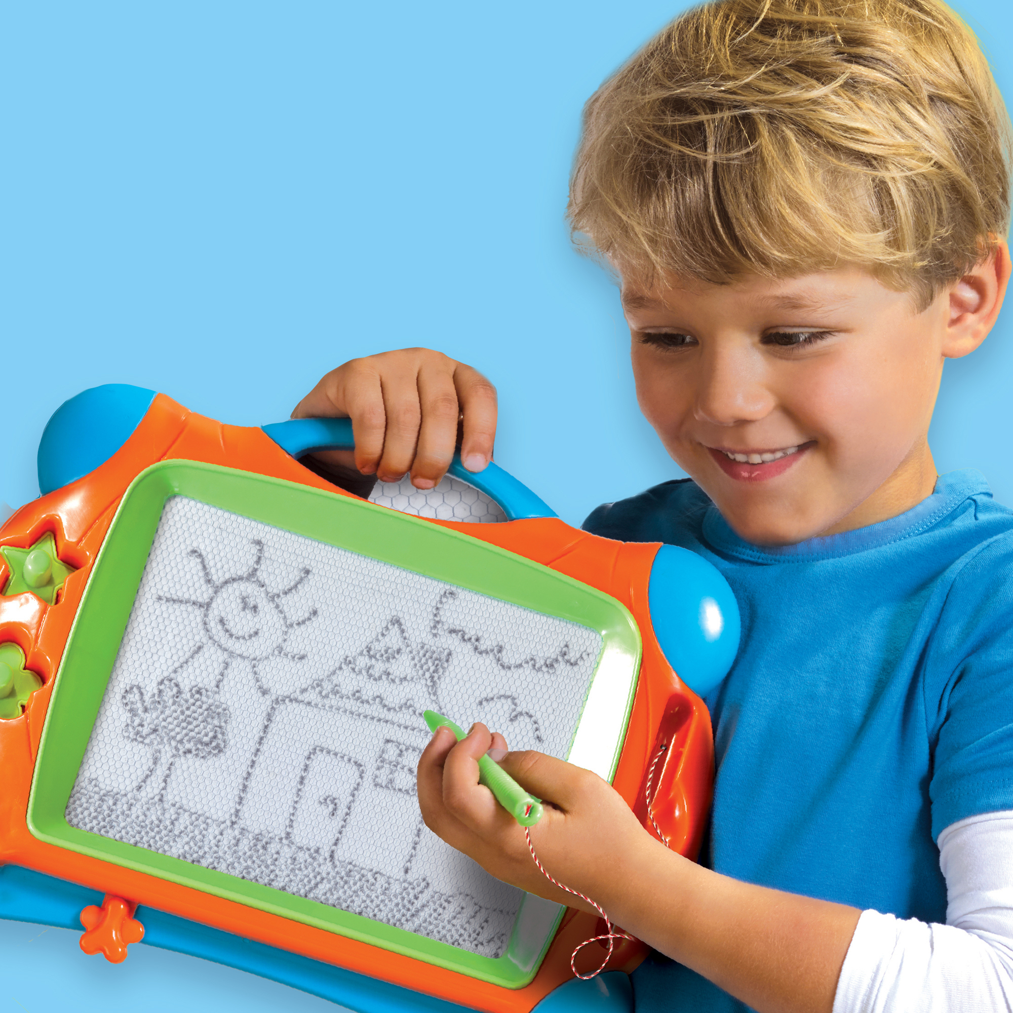 Chłopiec rysuje na magnetycznej tablicy. Rysuje dom i słońce. Tablica jest pomarańczowa, zielona i niebieska.