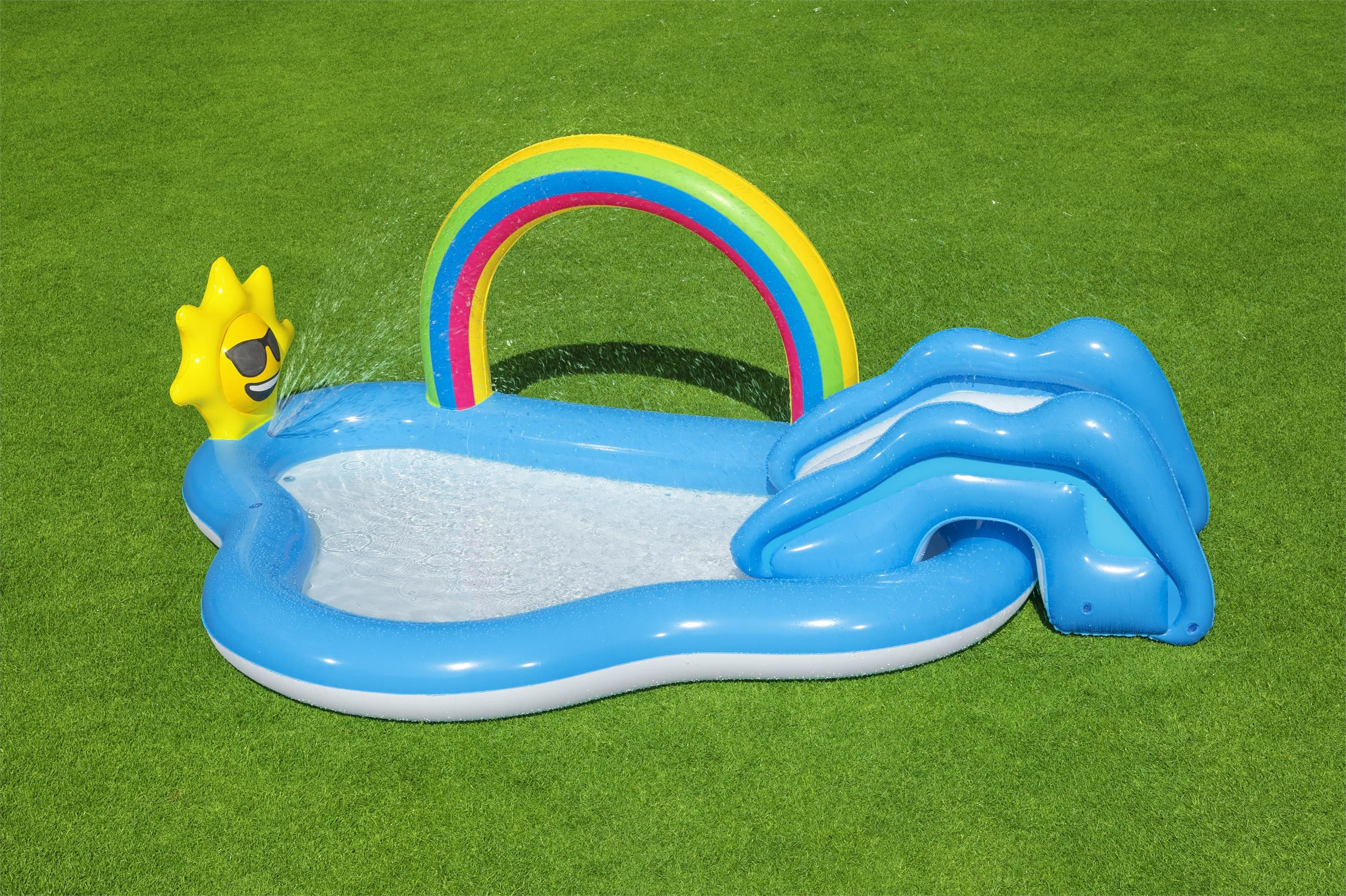 Una piscina inflable para niños con forma de ballena y un arcoíris. El fondo es césped verde.