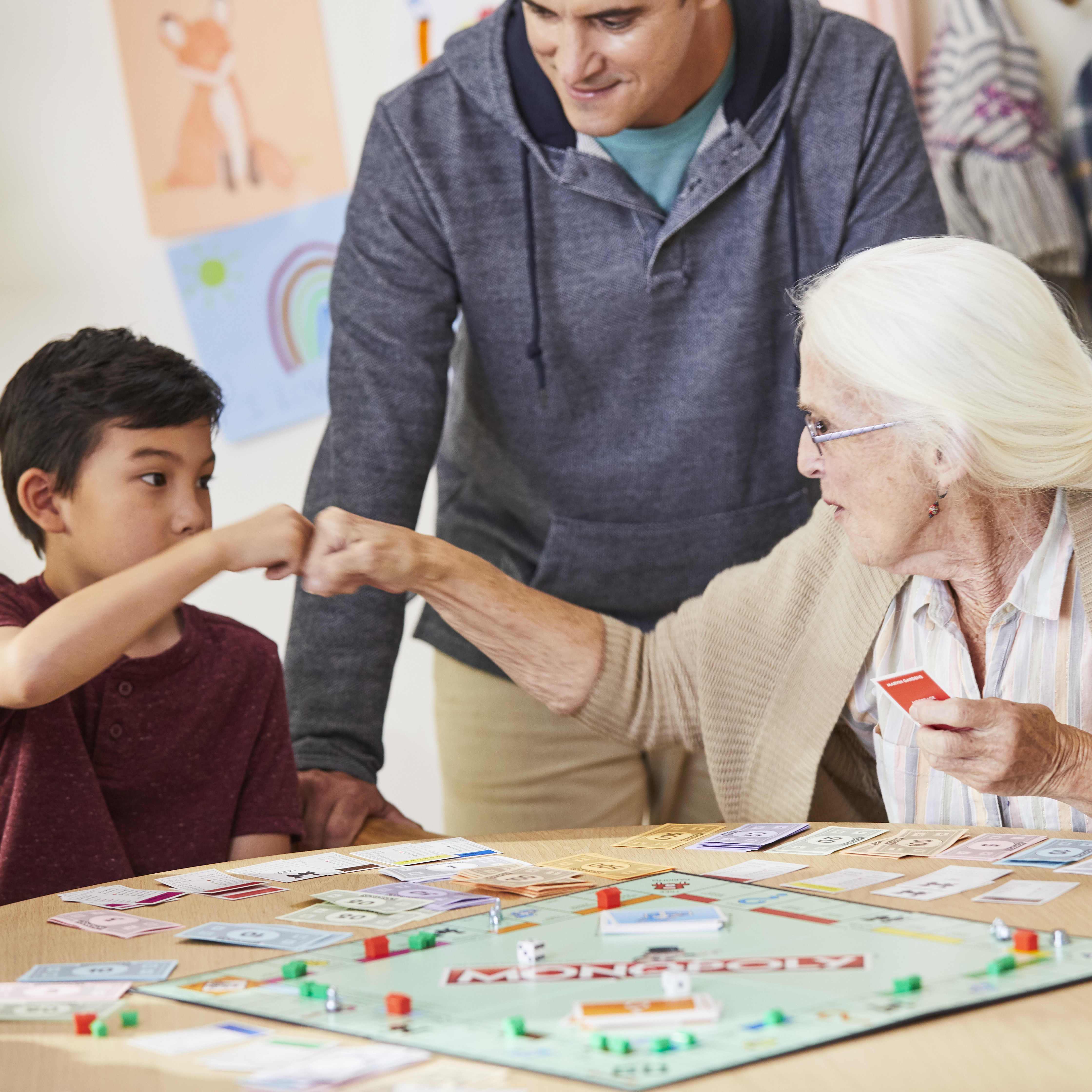 Chłopiec, kobieta i mężczyzna grają w Monopoly. Dają sobie piątkę. Plansza i pieniądze są na stole.