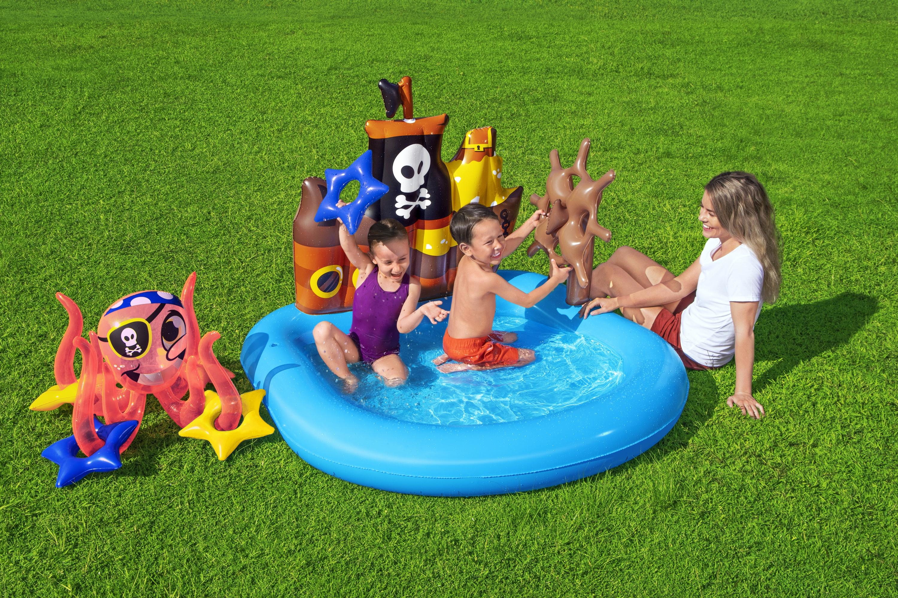 Kinder in einem Pool mit aufblasbarem Spielzeug und eine Frau, die auf Gras sitzt.