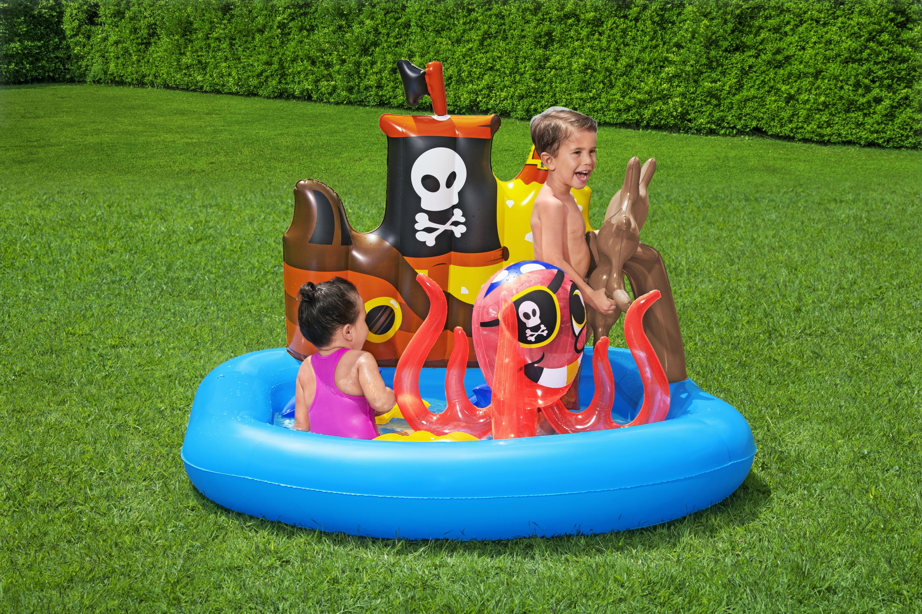 Kinder in einem Pool mit Piratenmotiv. Einer trägt rosa Badekleidung, der andere ist oben ohne. Aufblasbare Artikel: Oktopus, Schiff und Gras.