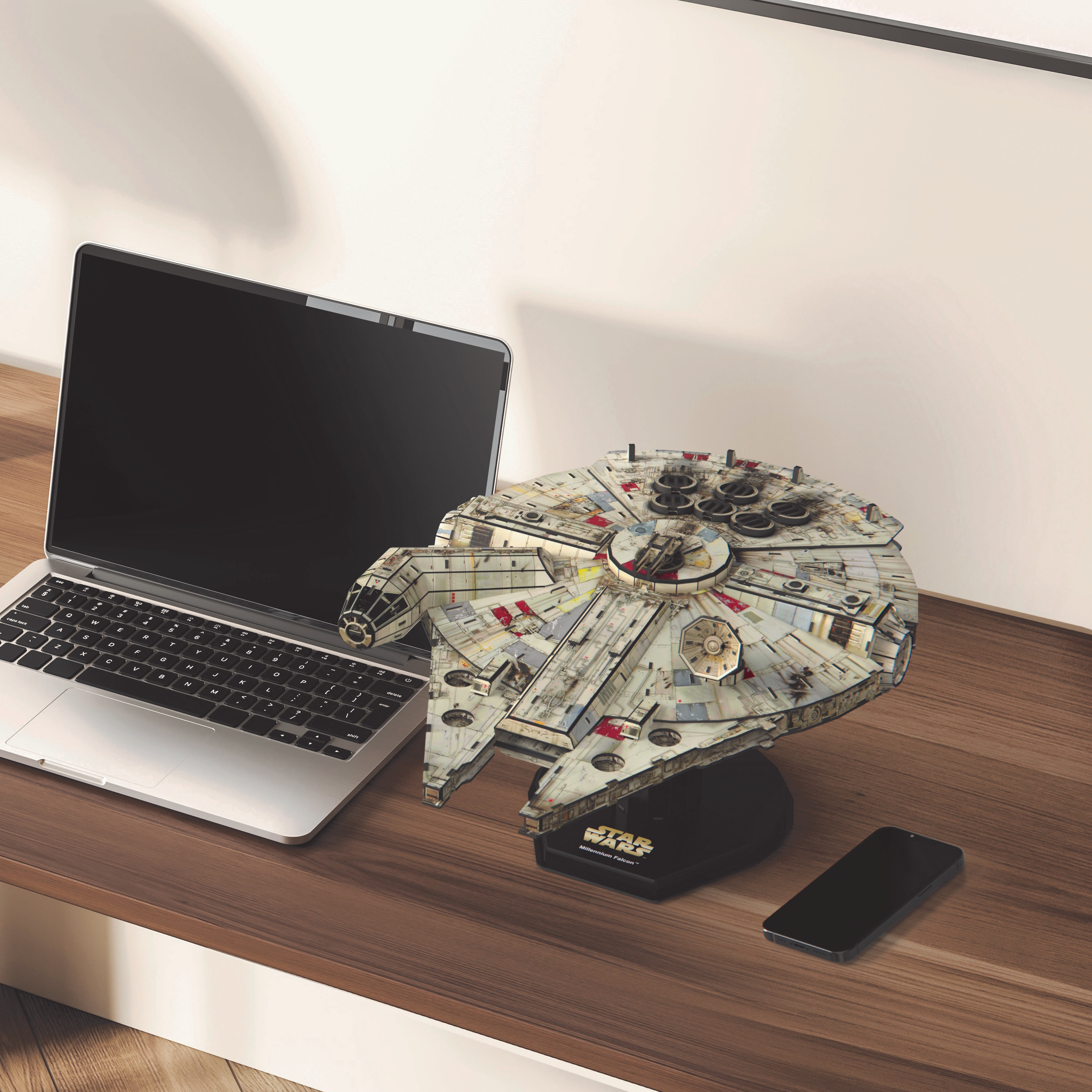 Laptop, model Star Wars Millennium Falcon i smartfon na drewnianym biurku.