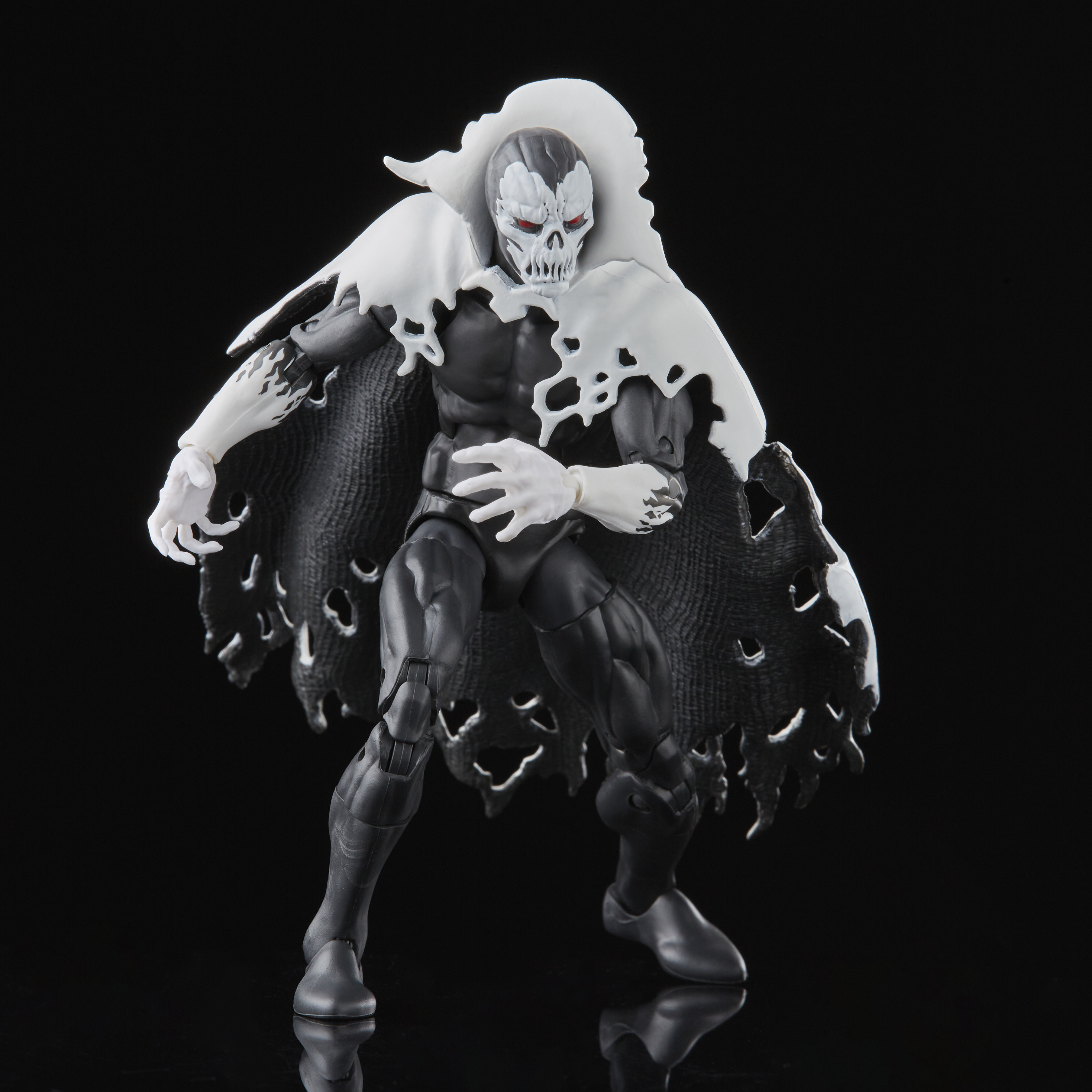 Figura di un personaggio scheletrico in abito nero e mantello bianco, volto a teschio e occhi rossi, su sfondo nero.
