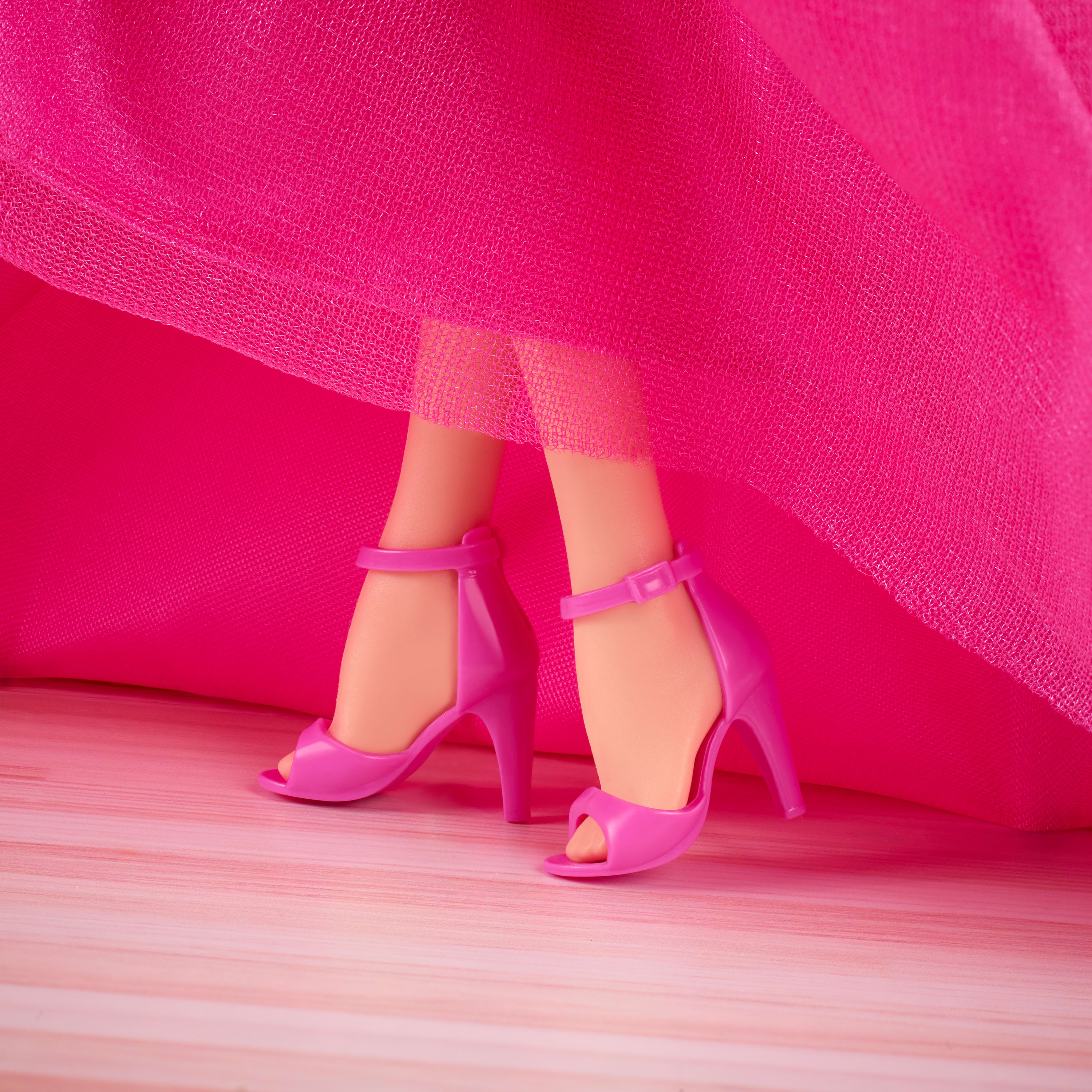 Nahaufnahme von Puppenbeinen und rosa High Heels. Die Beine der Puppe sind hellhäutig. Rosa Stoff drapiert sich um sie.