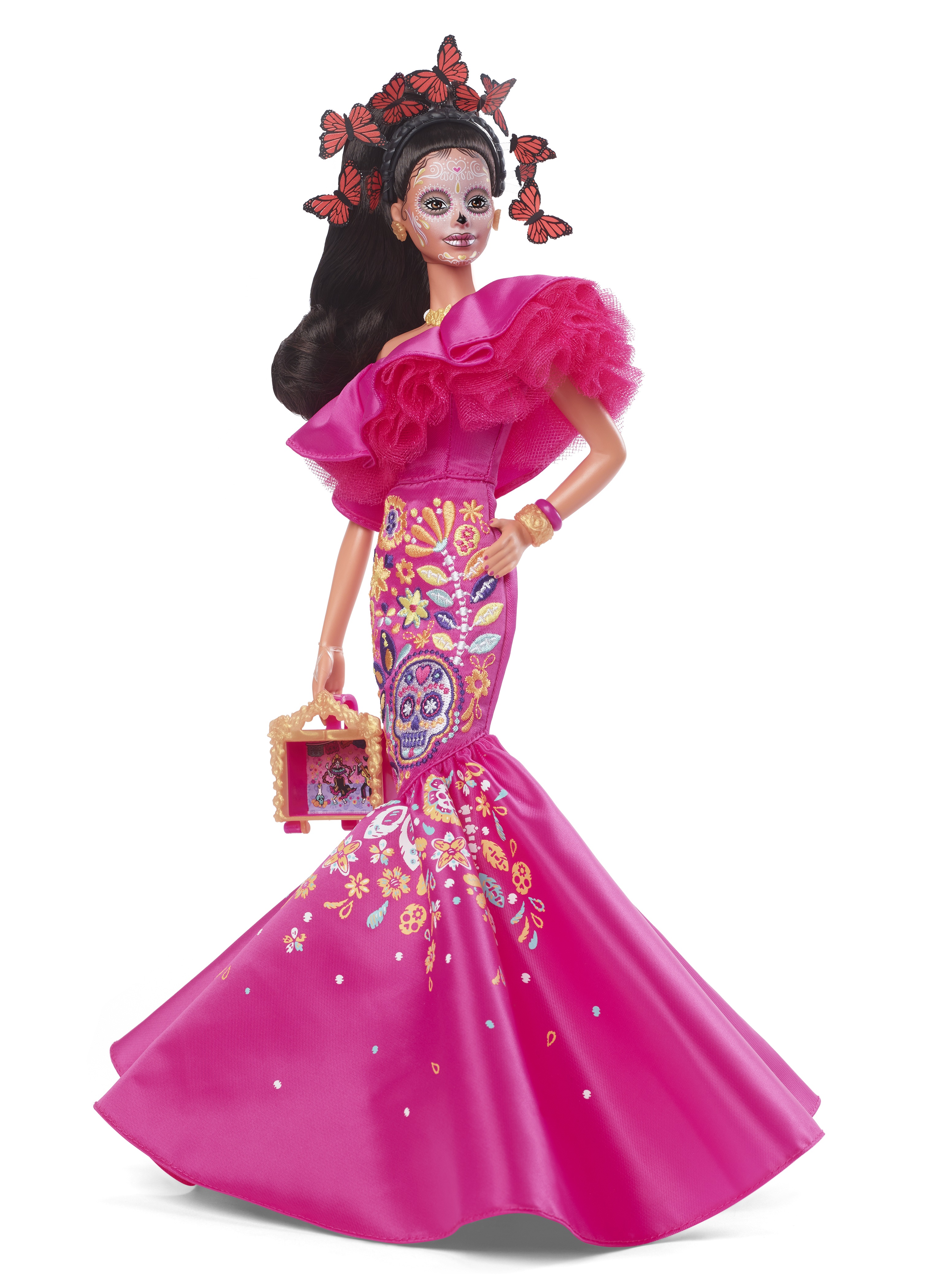 Eine Barbie-Puppe in einem rosa Kleid, mit Schmetterlings-Haarschmuck und Gesichtsbemalung, hält ein kleines gerahmtes Bild.