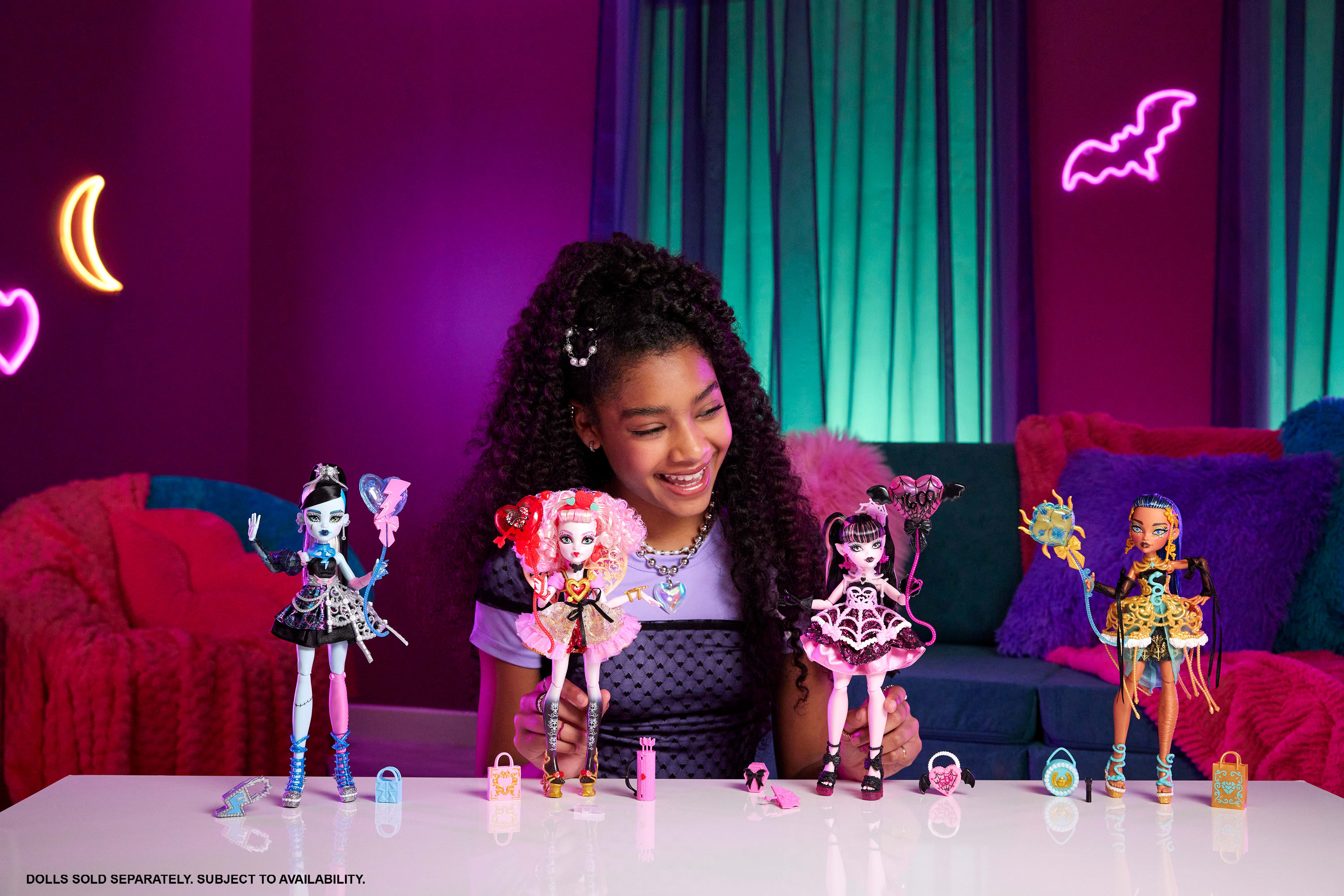 Una niña sonríe, sosteniendo muñecas de Monster High. Letreros de neón morados y muñecas están sobre una mesa blanca. Tema rosa y morado.