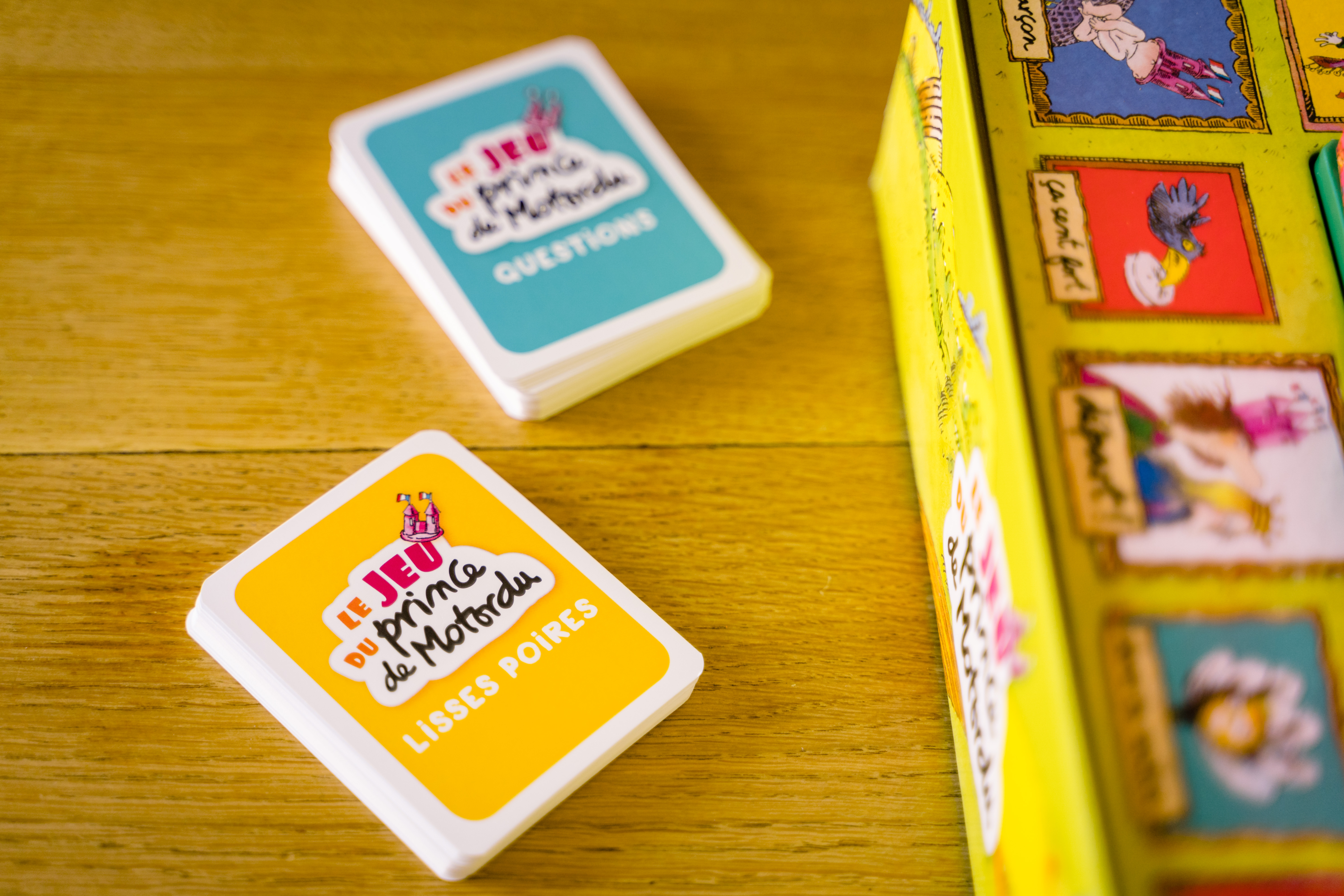 Un gioco con carte e una scatola gialla. Le carte hanno testo francese, la scatola ha illustrazioni. Sfondo tavolo in legno.