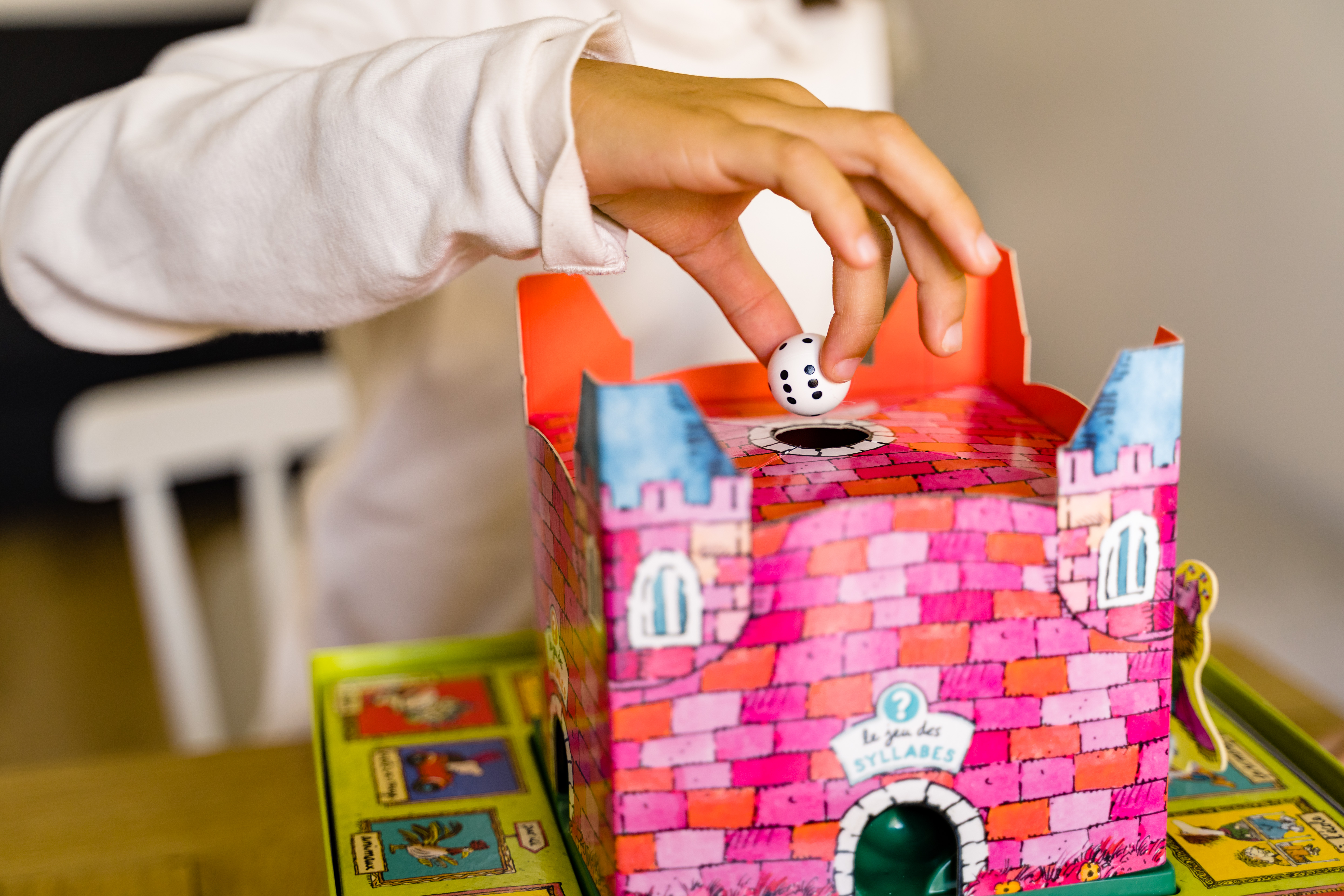 Una mano lascia cadere un dado in un gioco del castello rosa. Il dado è bianco con punti neri. Un tabellone è visibile.
