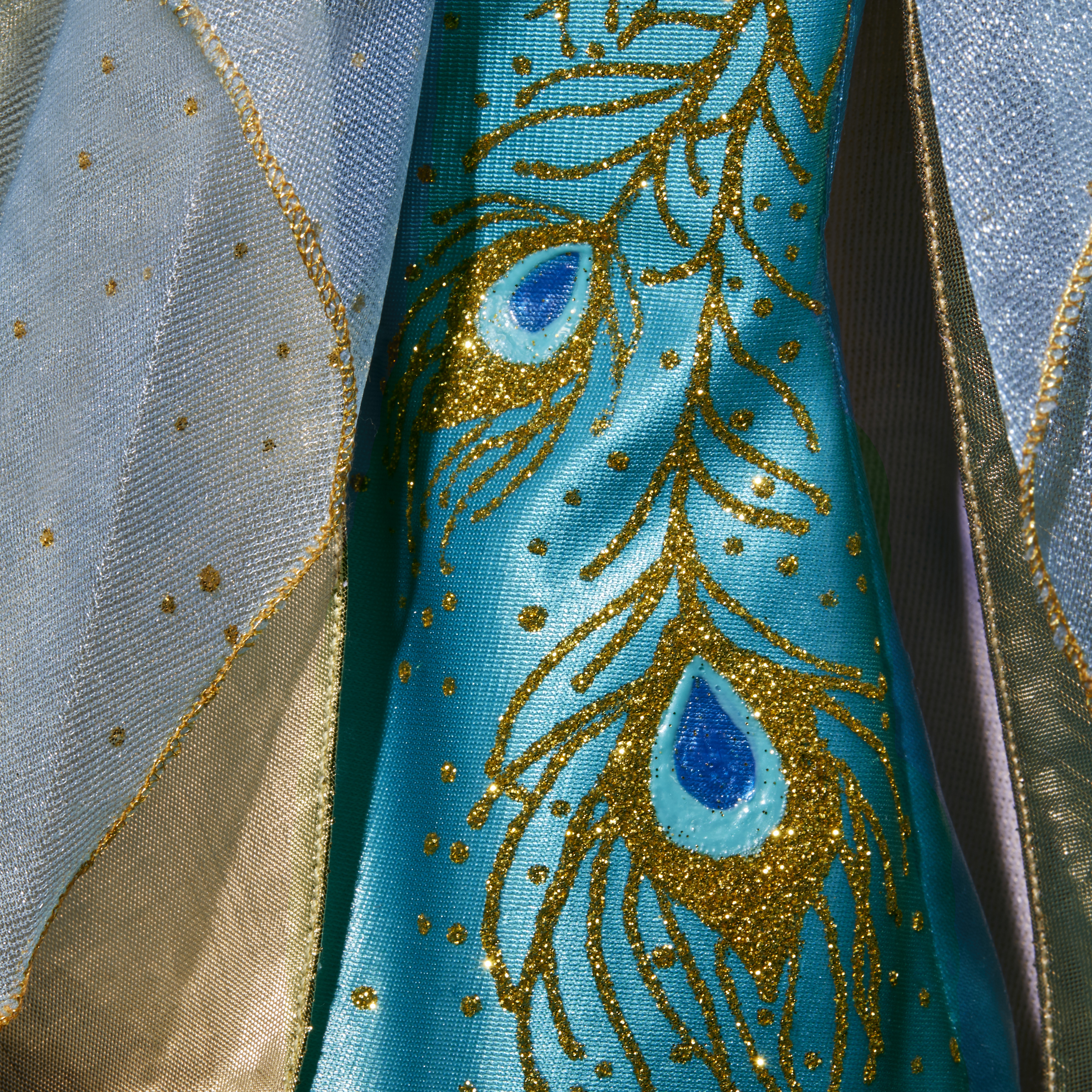 Nahaufnahme eines blauen Kleides, das mit goldenen Glitzer-Pfauenfedern und goldenen Verzierungen verziert ist.