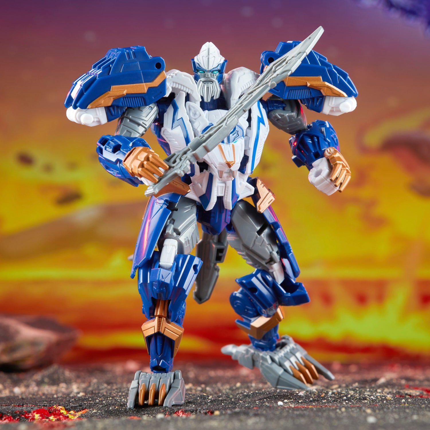 Un robot giocattolo blu e bianco tiene una spada d'argento. Accenti dorati su braccia e gambe. Lo sfondo è un cielo arancione.