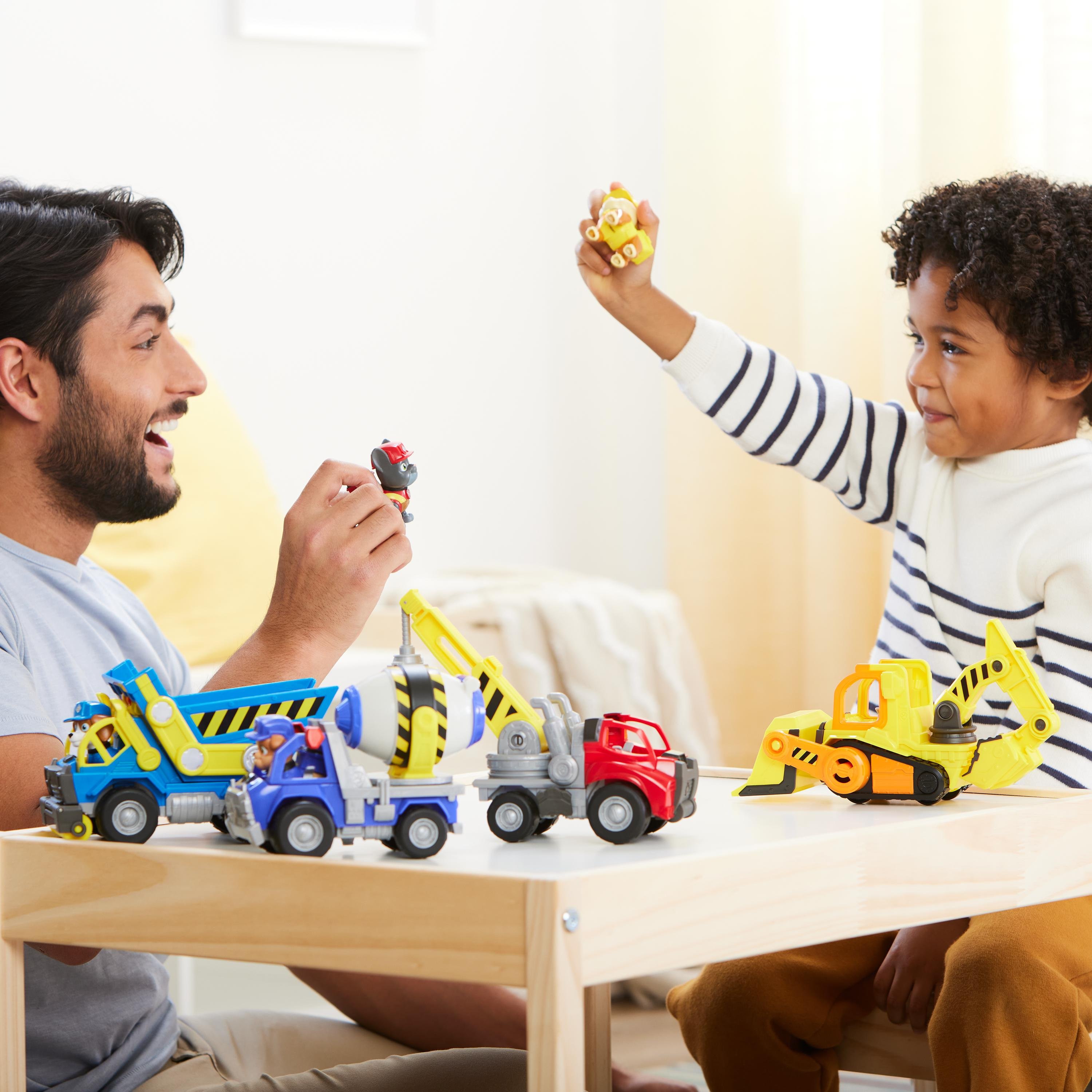 Mężczyzna i chłopiec bawią się zabawkowymi ciężarówkami. Chłopiec trzyma żółtą zabawkę. Mężczyzna trzyma czerwoną zabawkę.