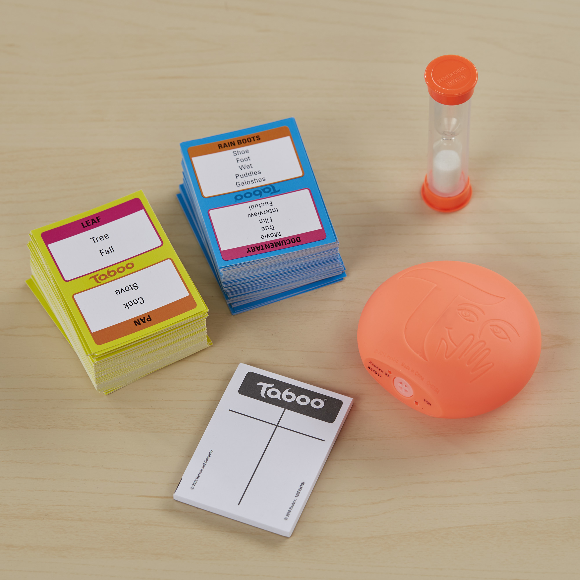 Taboo-spelset met kaarten, timer en zoemer op een houten oppervlak. Kaarten hebben woordaanwijzingen zoals 'regenlaarzen'.