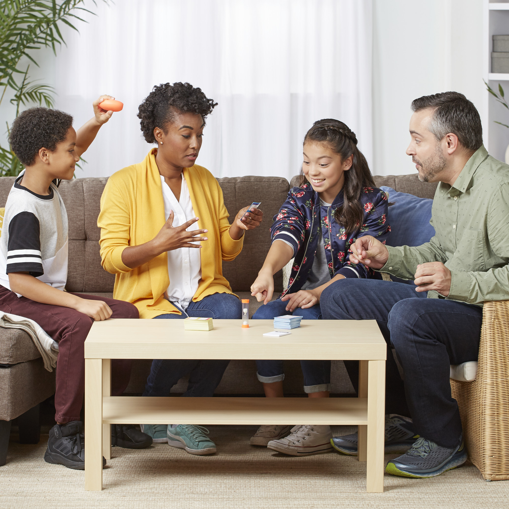 Familie speelt een spel. Mensen zitten rond een tafel. Kaarten, timer en een spelstuk zijn zichtbaar.