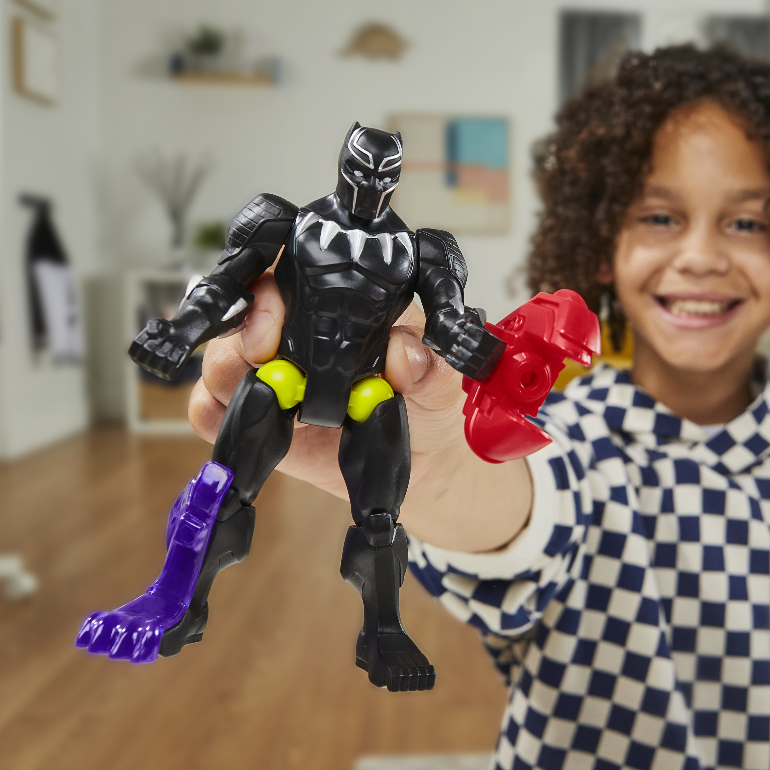 Un niño sostiene una figura de acción de Pantera Negra con un arma roja. El niño sonríe, usando una camisa a cuadros azul y blanca.