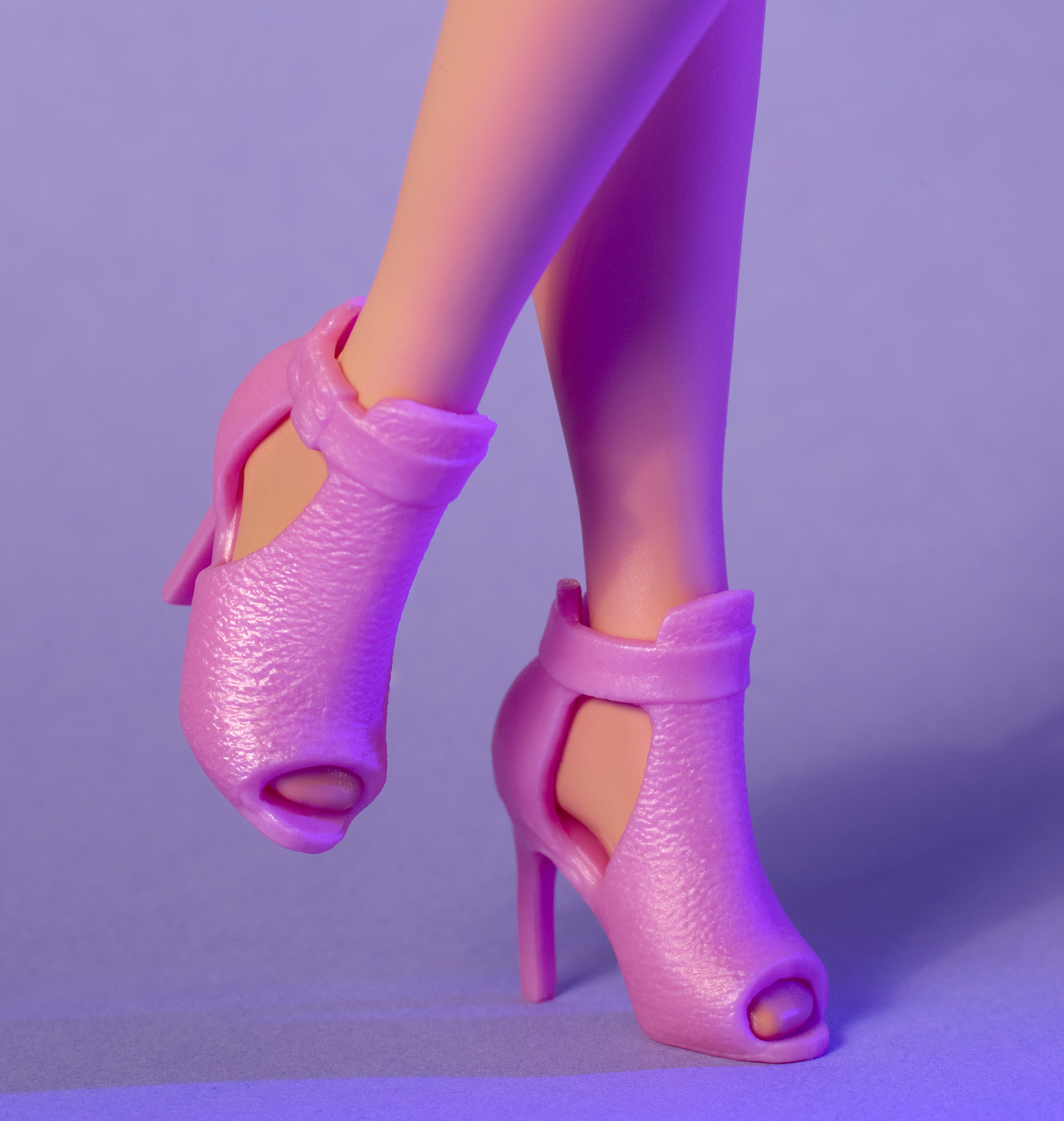 Różowe sandały na wysokim obcasie na stopach lalki na fioletowym tle. Sandały mają odkryte palce i paski.