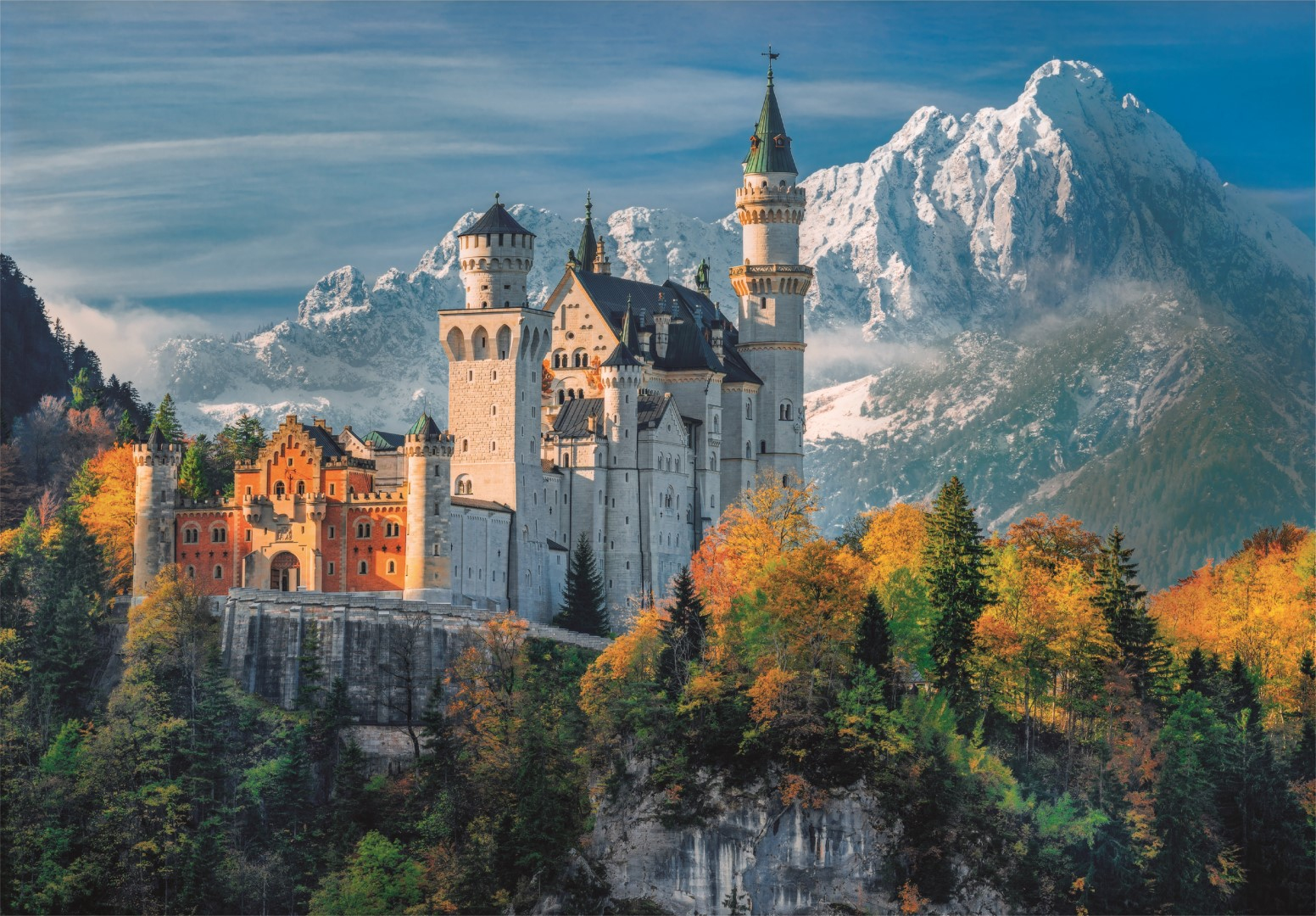 Schloss Neuschwanstein auf einem Hügel, umgeben von Bäumen mit Herbstfarben, schneebedeckte Berge im Hintergrund.