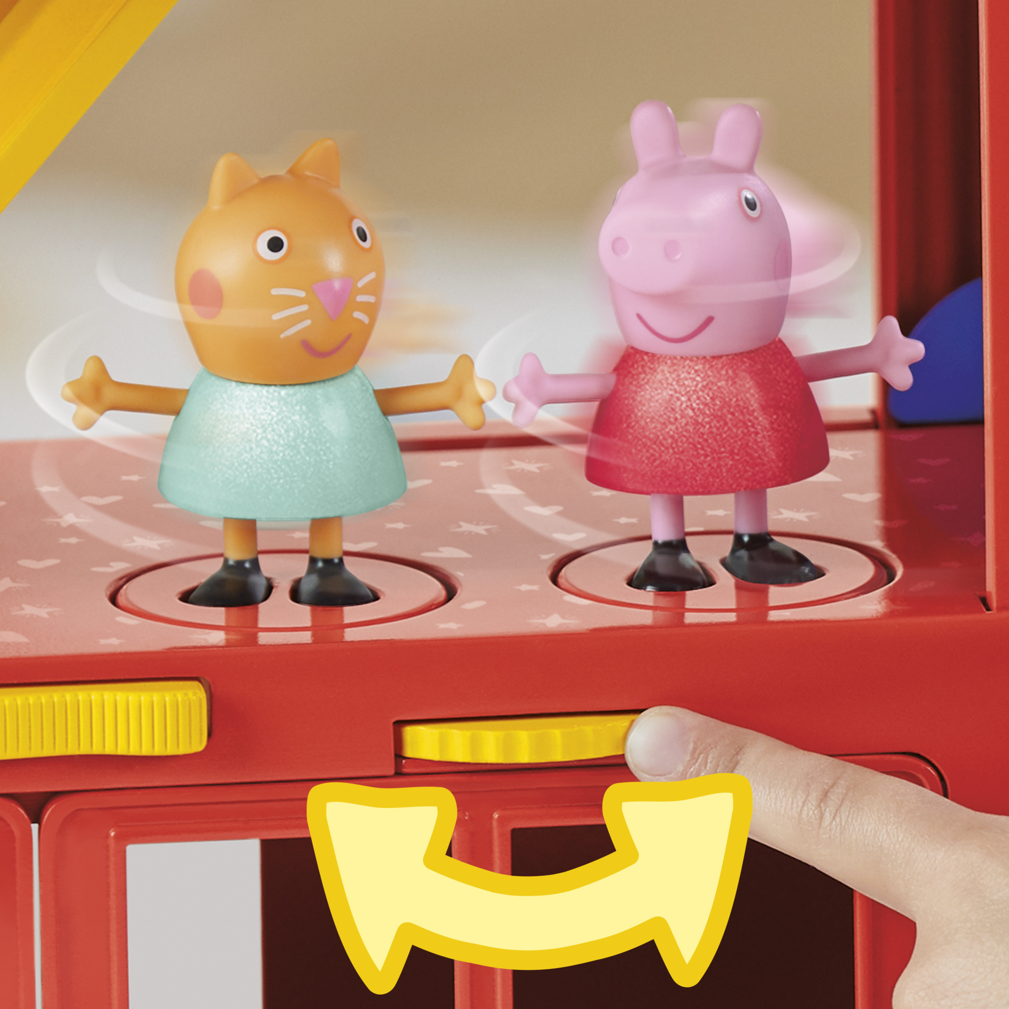 Autobús de juguete con figuras de Peppa Pig y gato. Una mano gira un dial amarillo. Autobús rojo, cerdo rosa, gato naranja.
