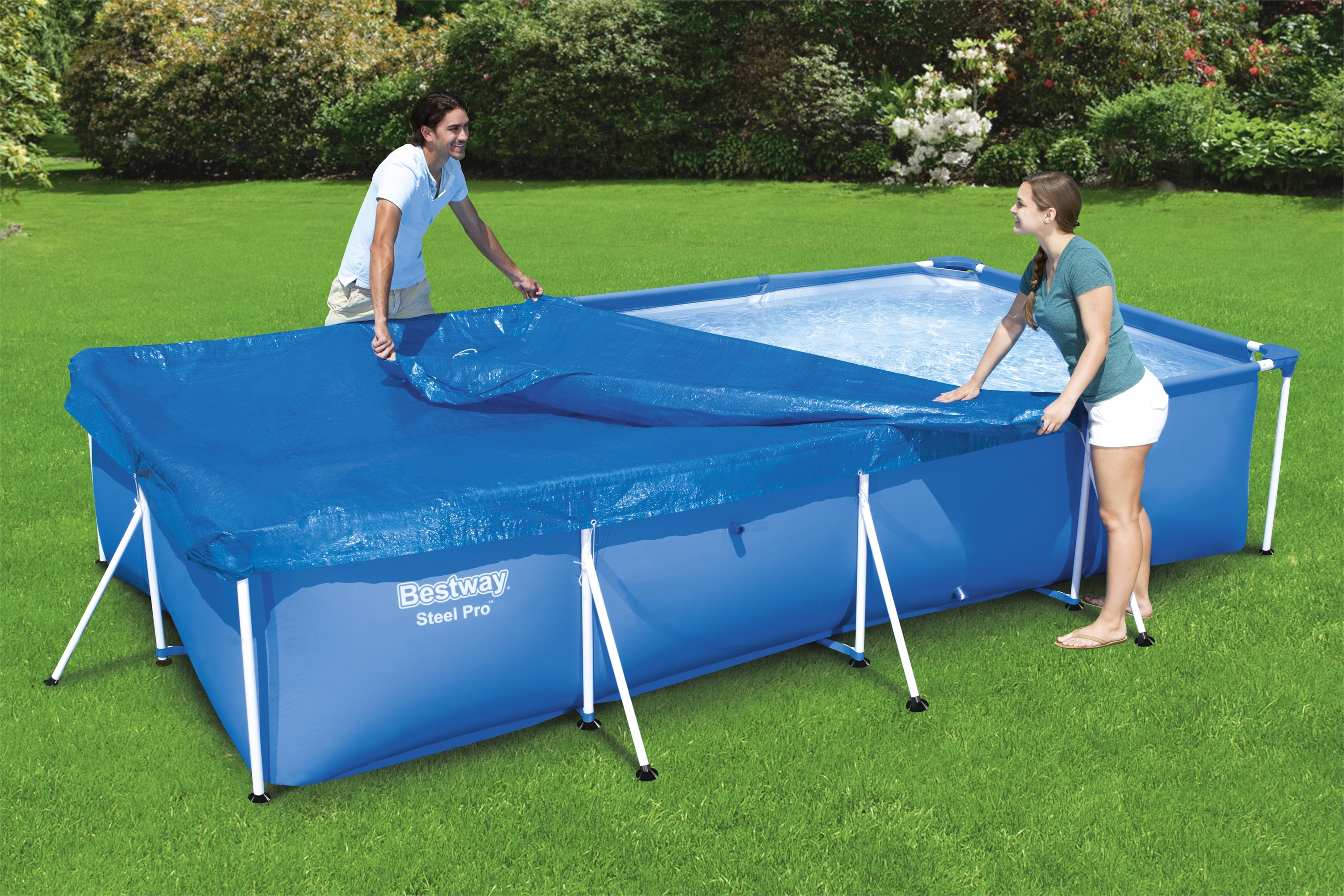 Zwei Personen decken einen blauen rechteckigen Pool mit einer blauen Abdeckung ab. Grüner Rasen umgibt den Pool.