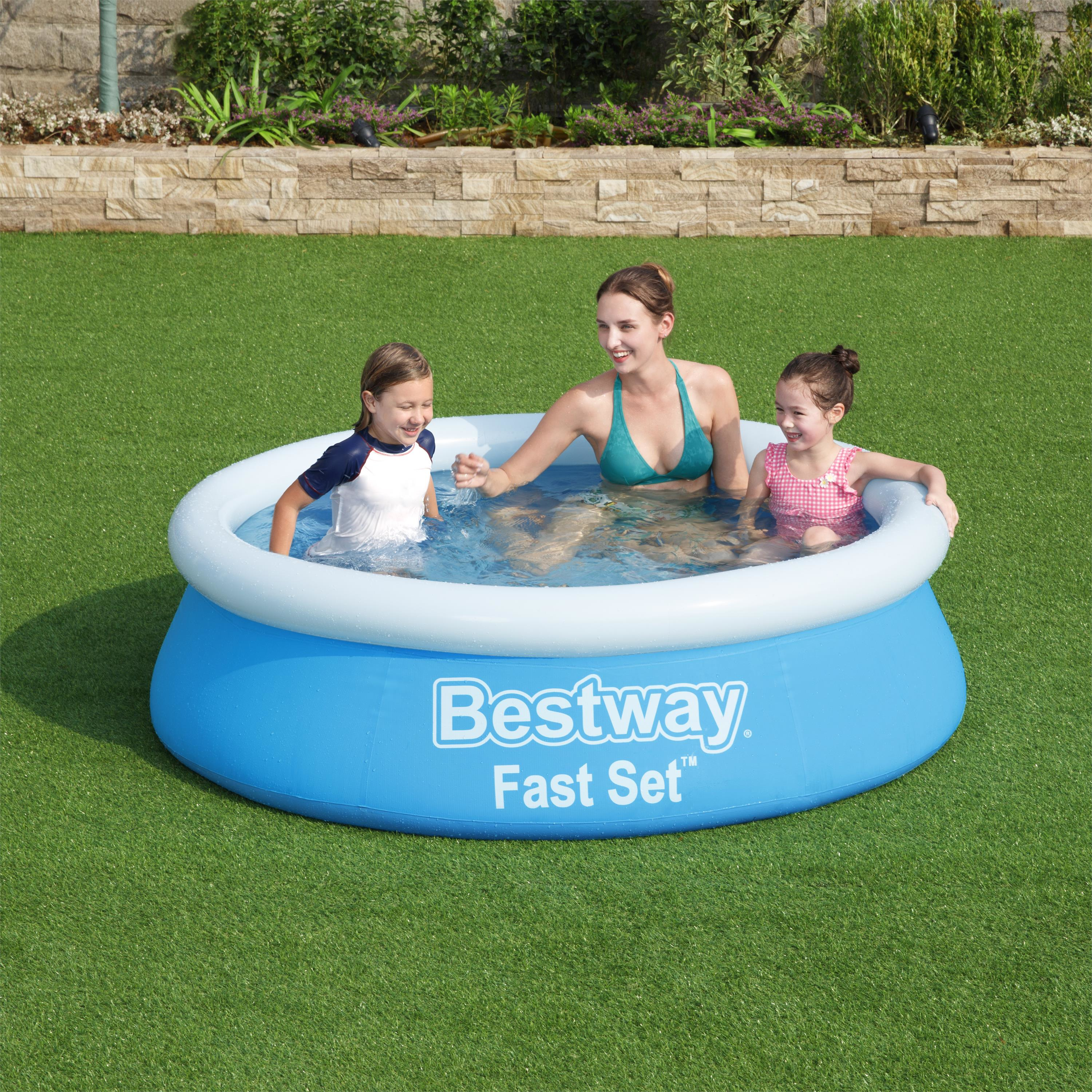 Eine Frau und zwei Mädchen in einem blauen Pool auf grünem Gras. Auf dem Pool steht 'Bestway Fast Set'.