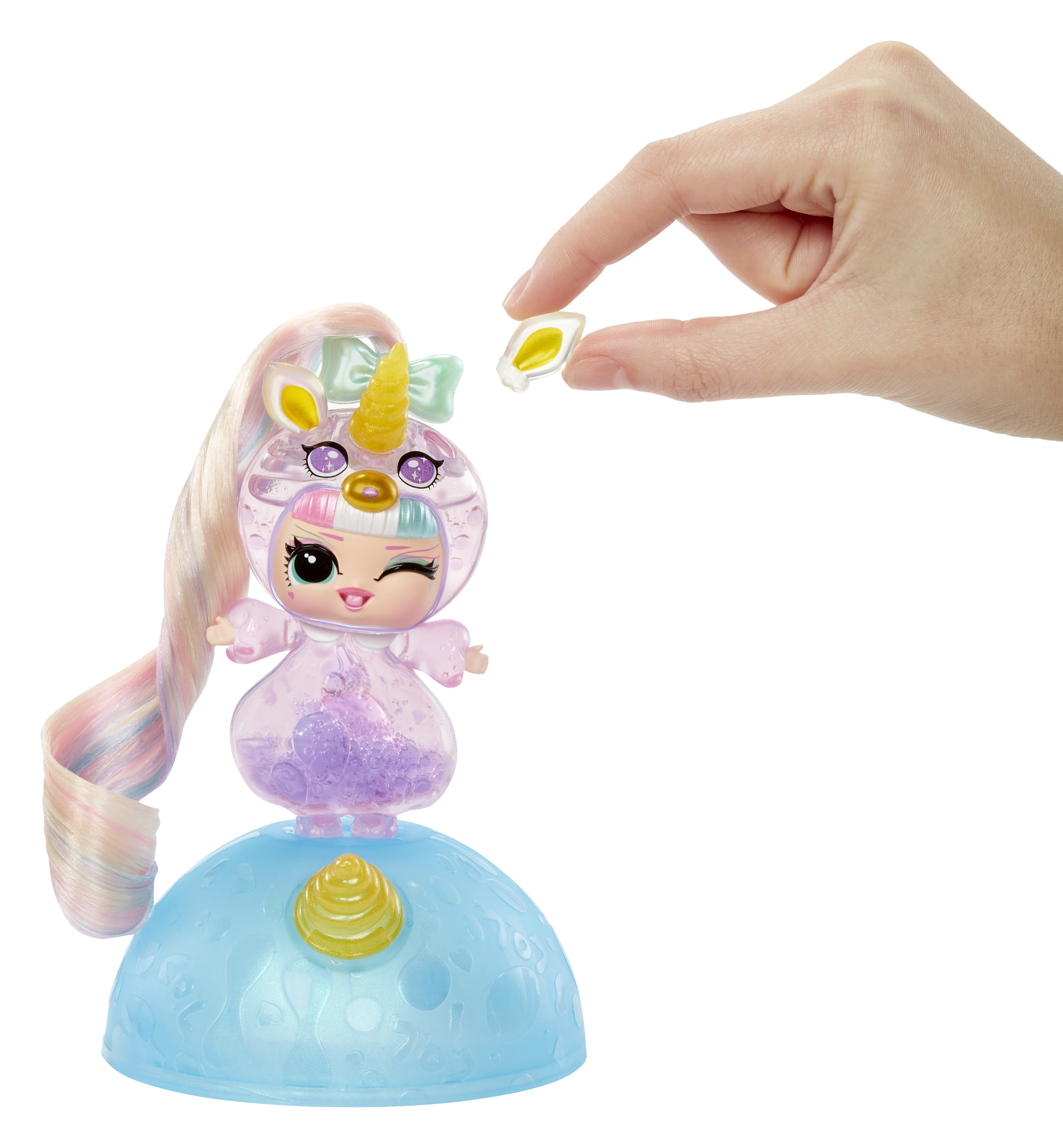Una muñeca con disfraz de unicornio es sostenida por una mano. La muñeca está sobre una base azul. Una pieza se sostiene sobre ella.