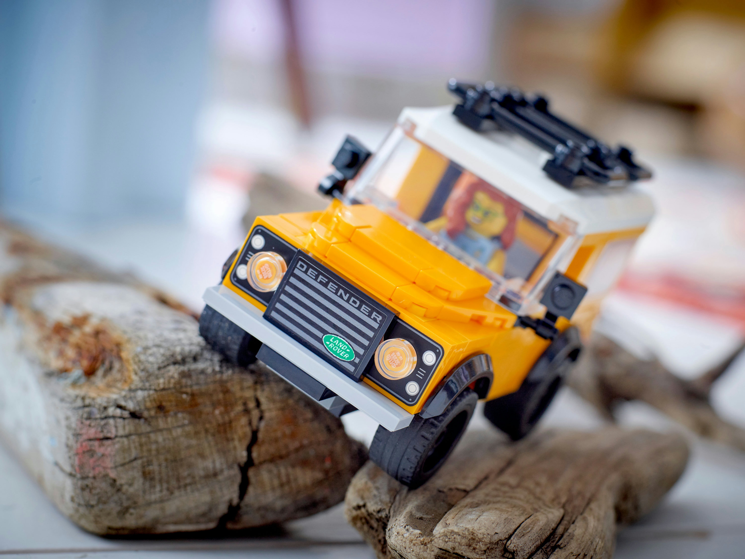 Ahşap yüzeyde sarı ve beyaz Lego Land Rover Defender oyuncağı. Defender logosu görünür.