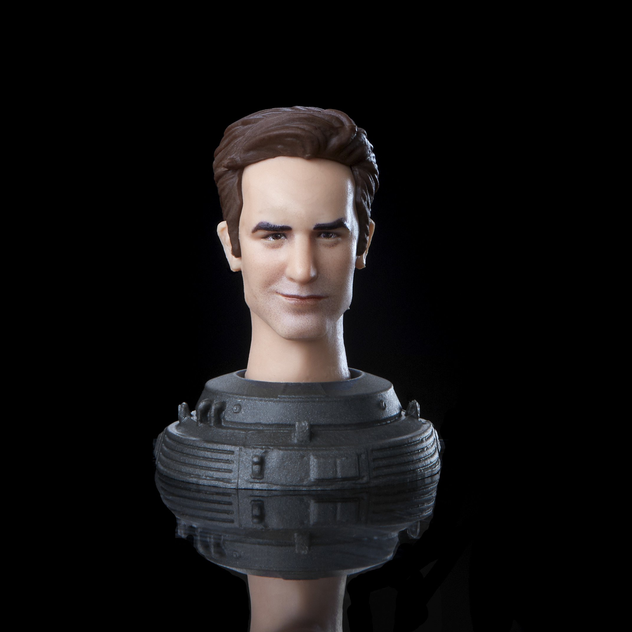 Un busto di un uomo con capelli castani e un leggero sorriso. Indossa un colletto grigio scuro, su sfondo nero.