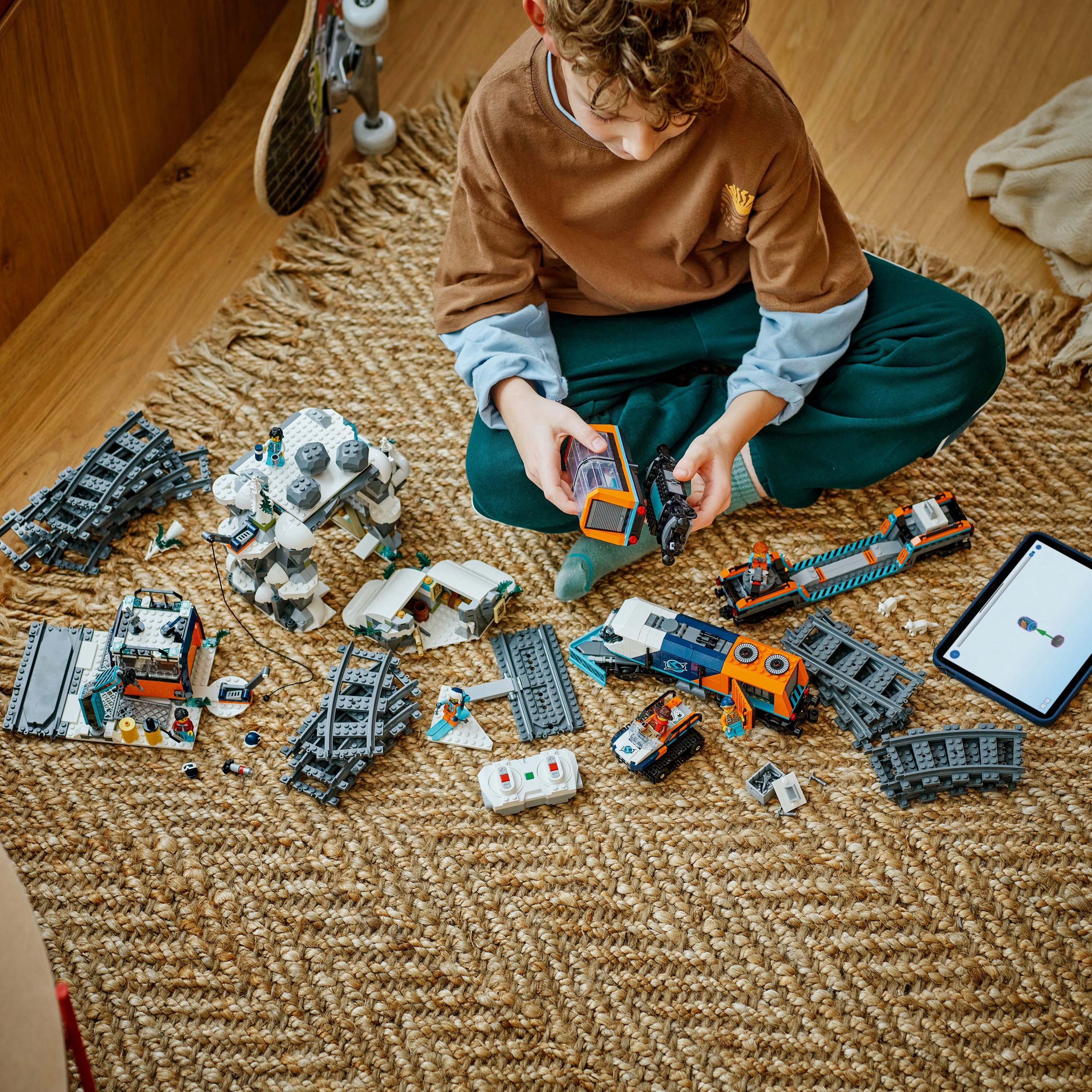 Dziecko bawi się torami i zestawami pociągów Lego na tkanym dywanie. Po prawej stronie znajduje się tablet.