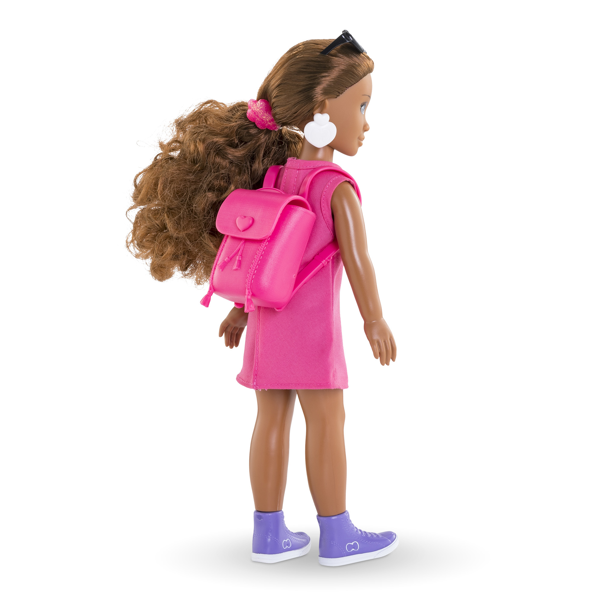 Eine Puppe mit rosa Kleid, Rucksack und Turnschuhen. Sie hat braune Haare, eine Sonnenbrille und weiße herzförmige Ohrringe.