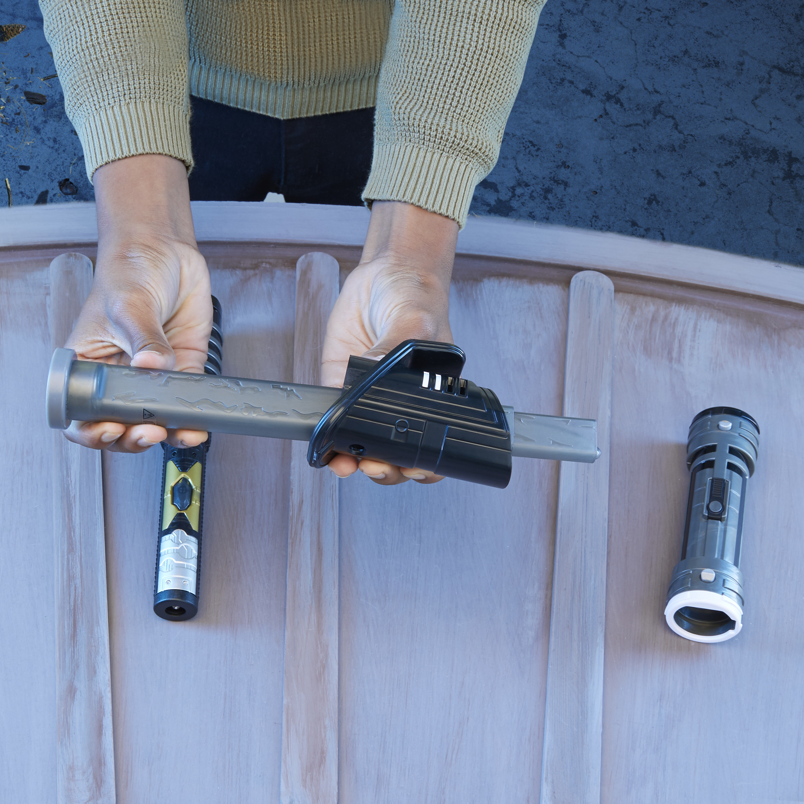 Le mani tengono un dispositivo grigio con un componente nero sopra una superficie di legno chiaro. Altri due dispositivi sono sulla superficie.