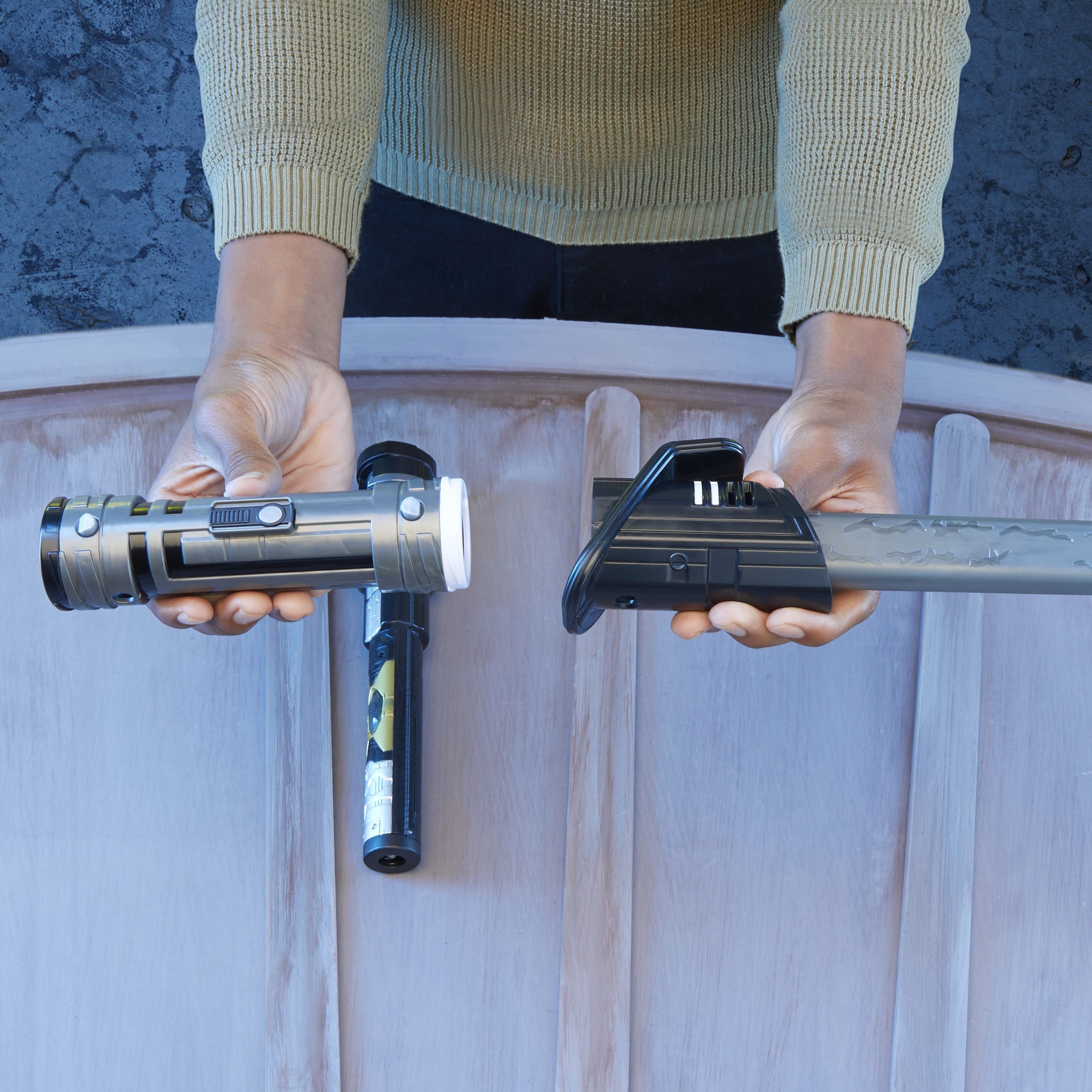 Le mani tengono due spade laser giocattolo su uno sfondo di legno. Una è argento, l'altra nera.