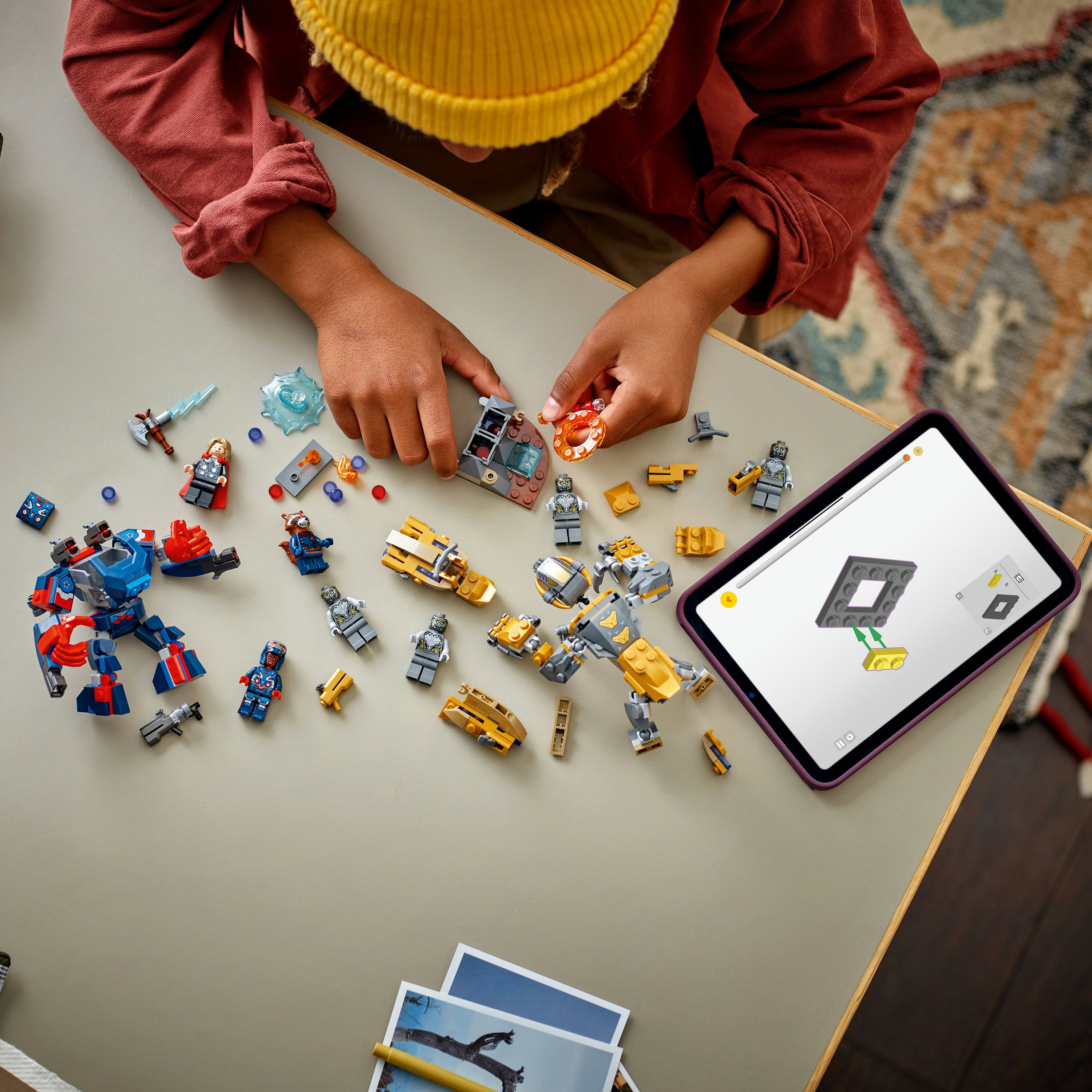 Dziecko składa Lego. Na stole znajdują się różne figurki i elementy Lego, a także tablet z instrukcjami.