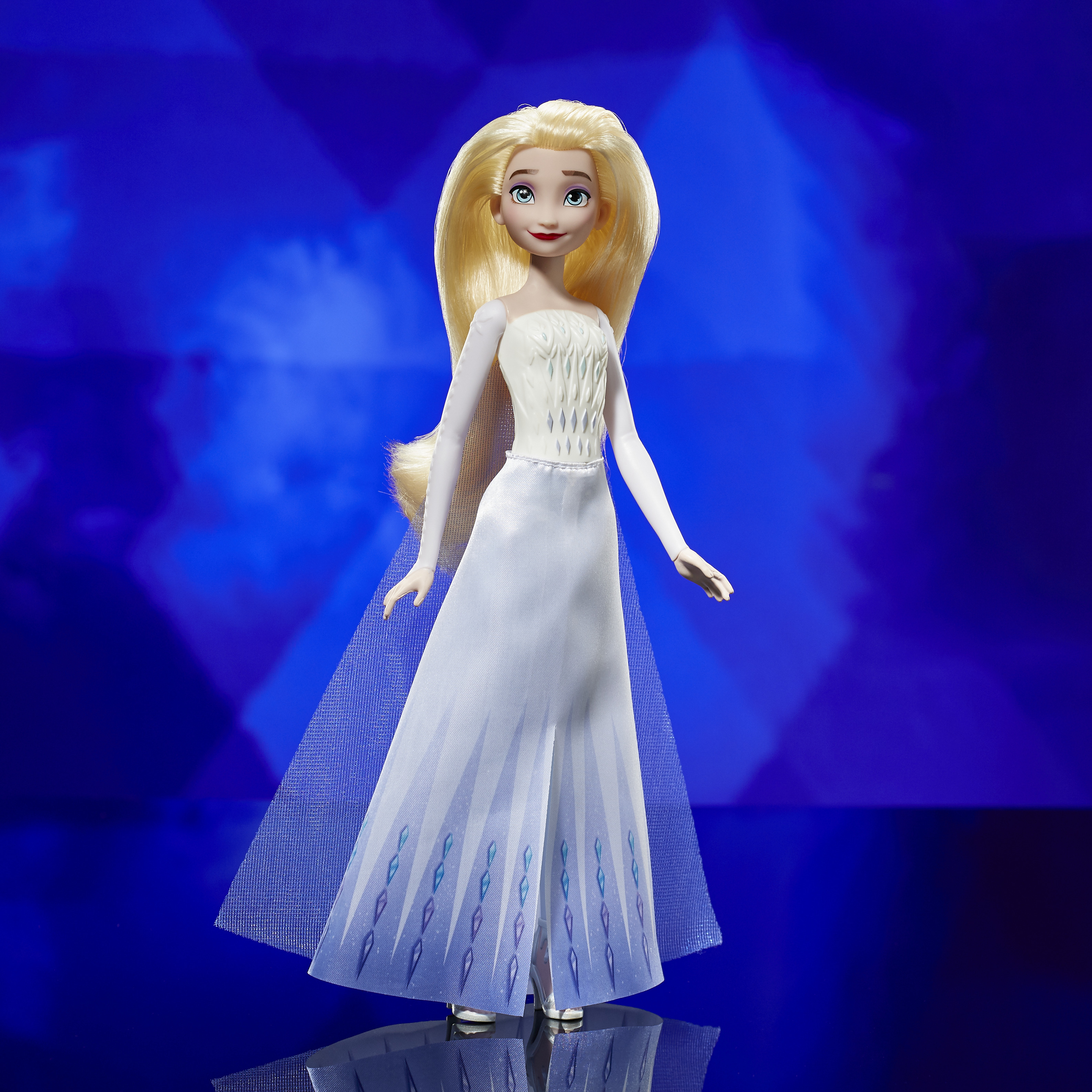 Eine Puppe von Elsa in einem weißen Kleid, mit langen blonden Haaren, vor blauem Hintergrund. Das Kleid hat Diamantenmuster.
