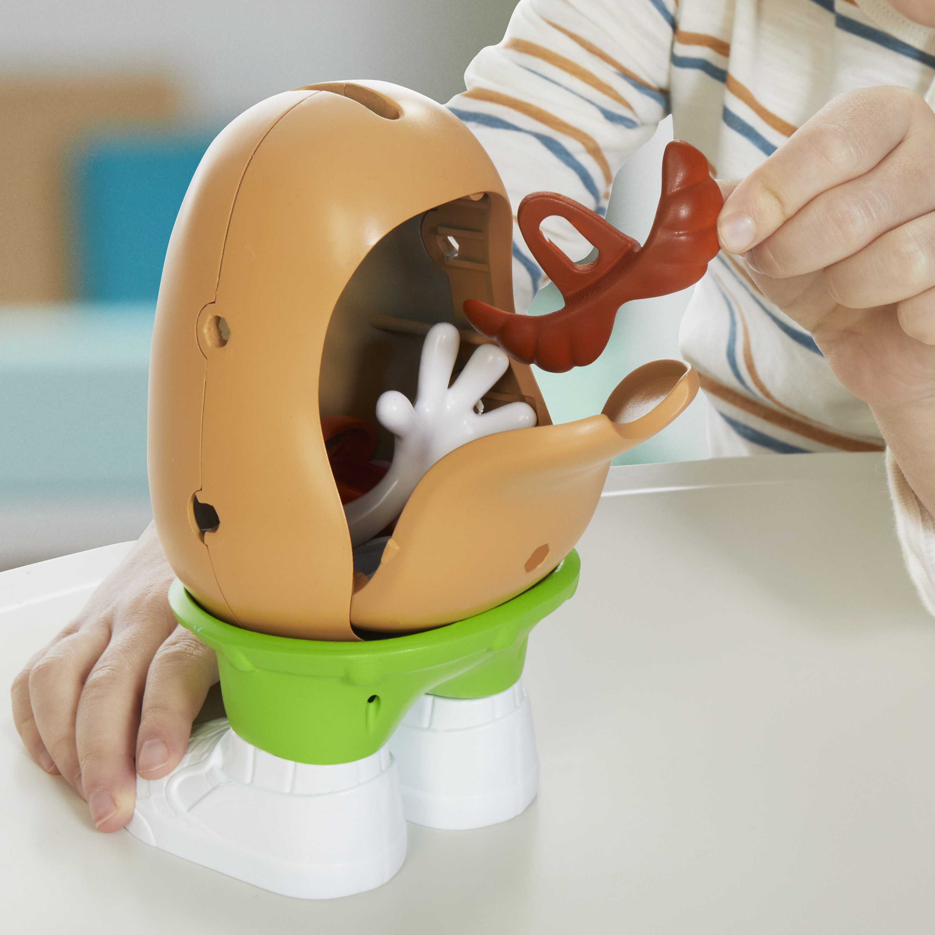 Un niño está montando un juguete de Mr. Potato Head. Se ven una cabeza marrón, una base verde y un accesorio rojo.