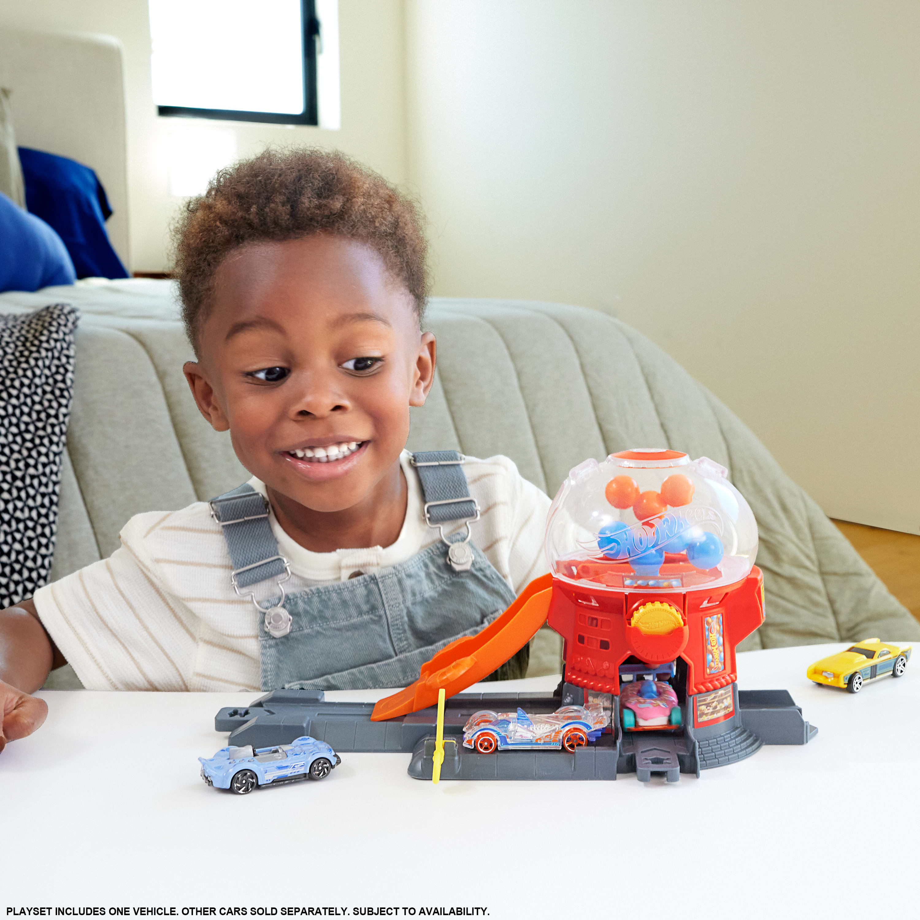 Chłopiec uśmiecha się do zestawu samochodowego z zabawkami. Zestaw zawiera konstrukcję podobną do automatu do gumy.