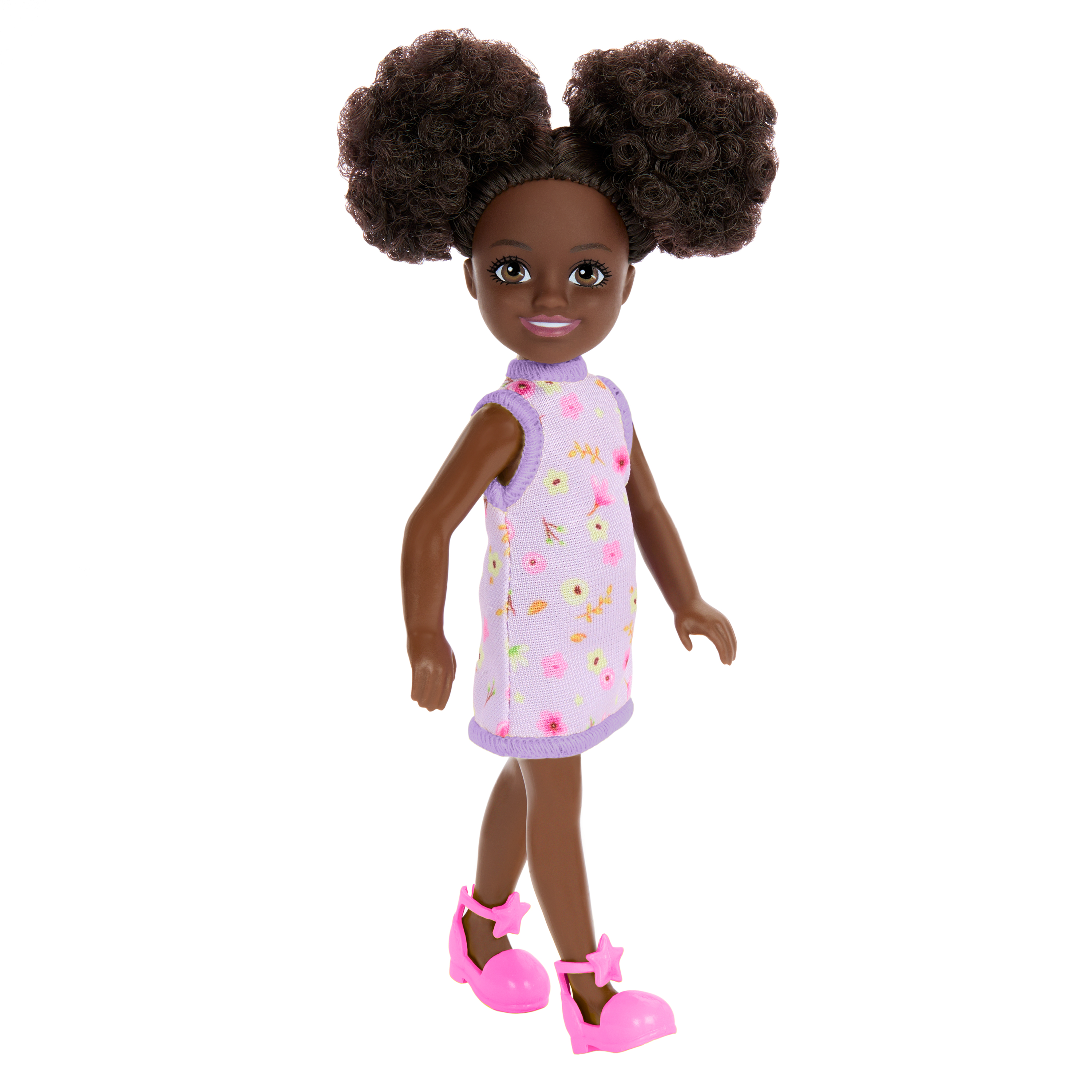 Puppe mit dunkler Haut, zwei Afro-Puffs und einem geblümten Kleid. Rosa Schuhe. Weißer Hintergrund.