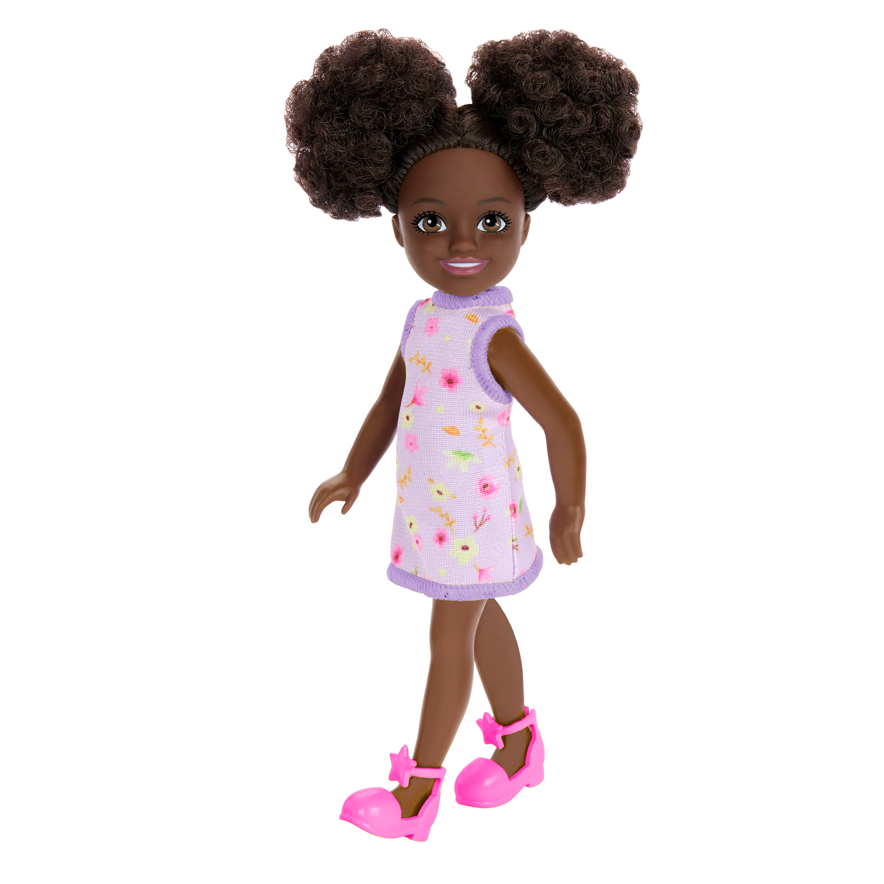 Eine Puppe mit dunkler Haut und Haaren in zwei Zöpfen. Sie trägt ein Blumenkleid und rosa Schuhe. Weißer Hintergrund.
